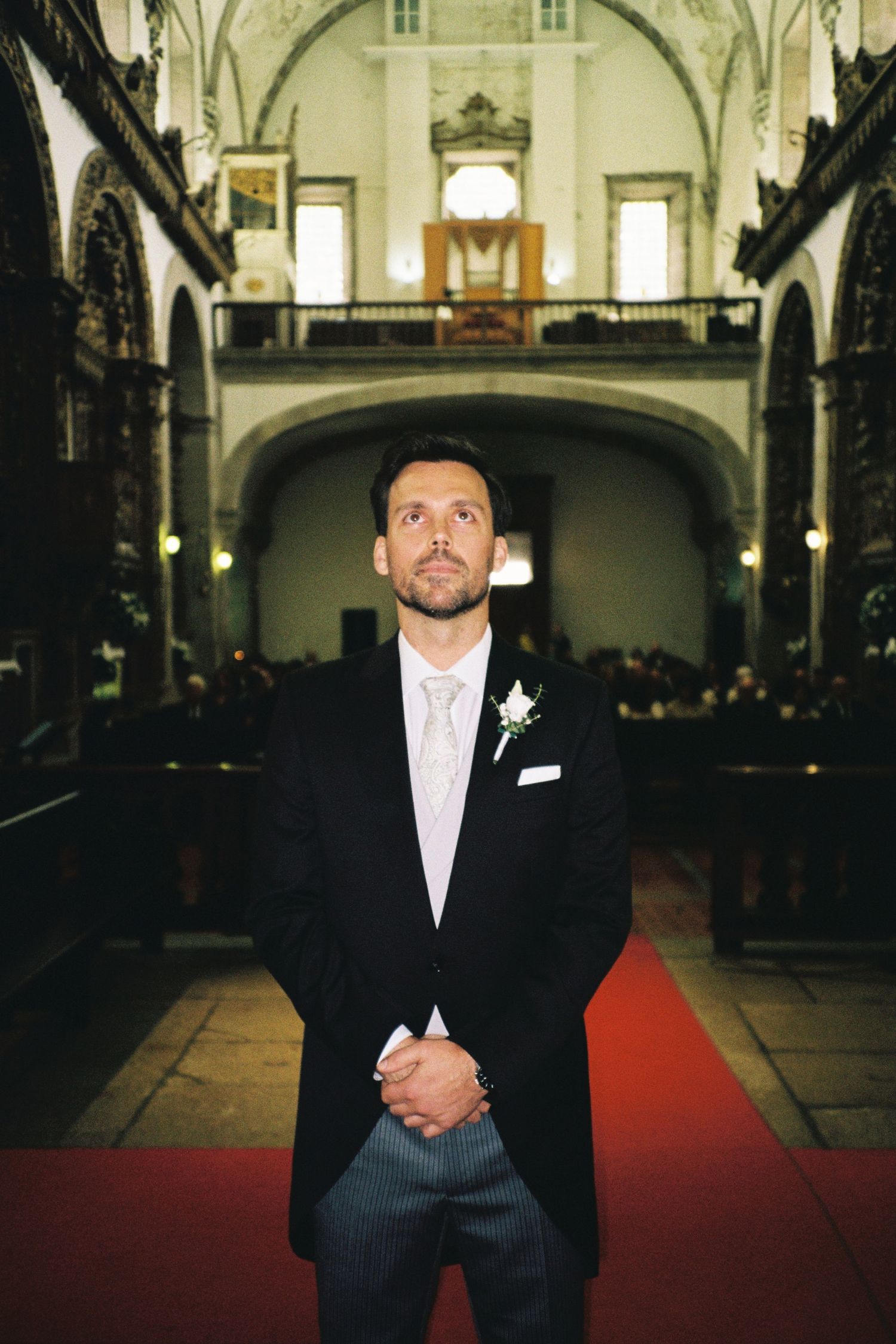 Groom standing solemnly at church altar on red carpet awaiting bride's arrival.