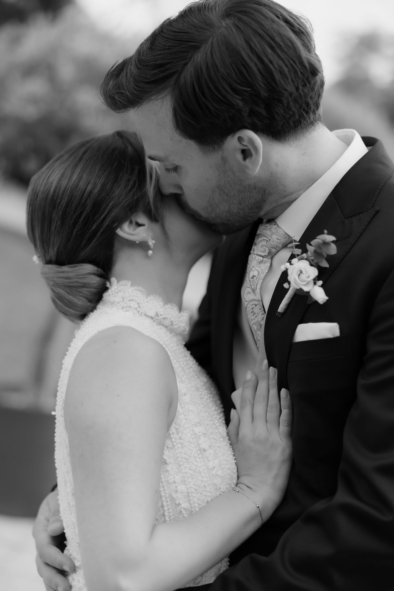 Black and white photo of bride and groom sharing intimate moment, groom kissing bride on forehead.