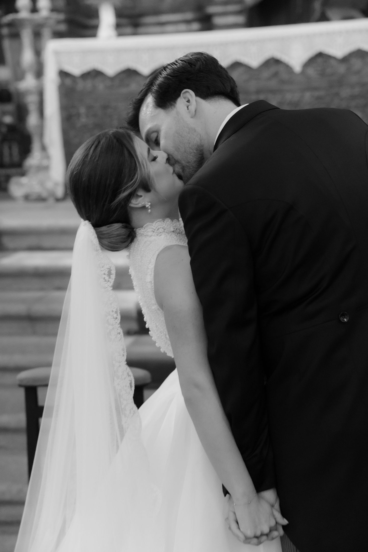 Black and white photo of newlyweds sharing a tender kiss at the church altar.