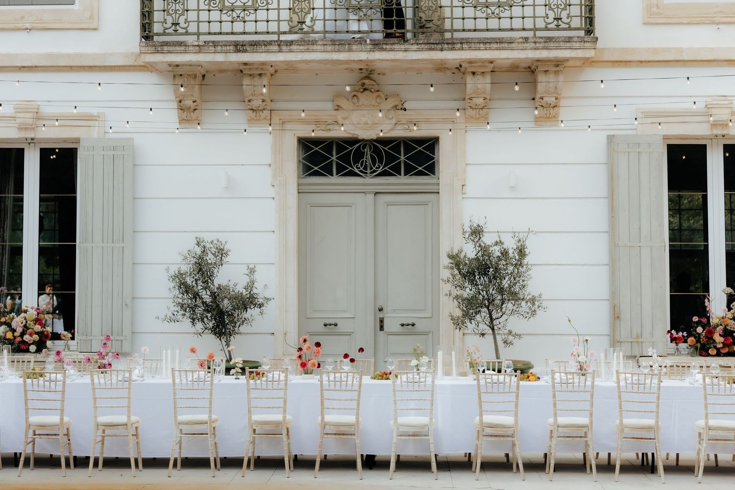 Elegant white wedding reception setup with chairs and floral arrangements along a classic building exterior.