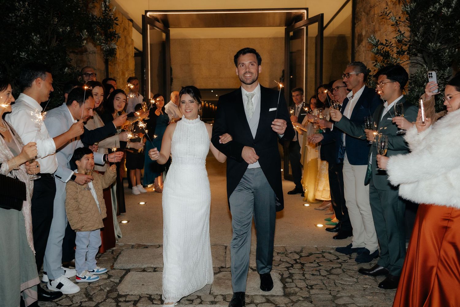 Bride and groom making grand exit through sparkler tunnel surrounded by cheering guests.
