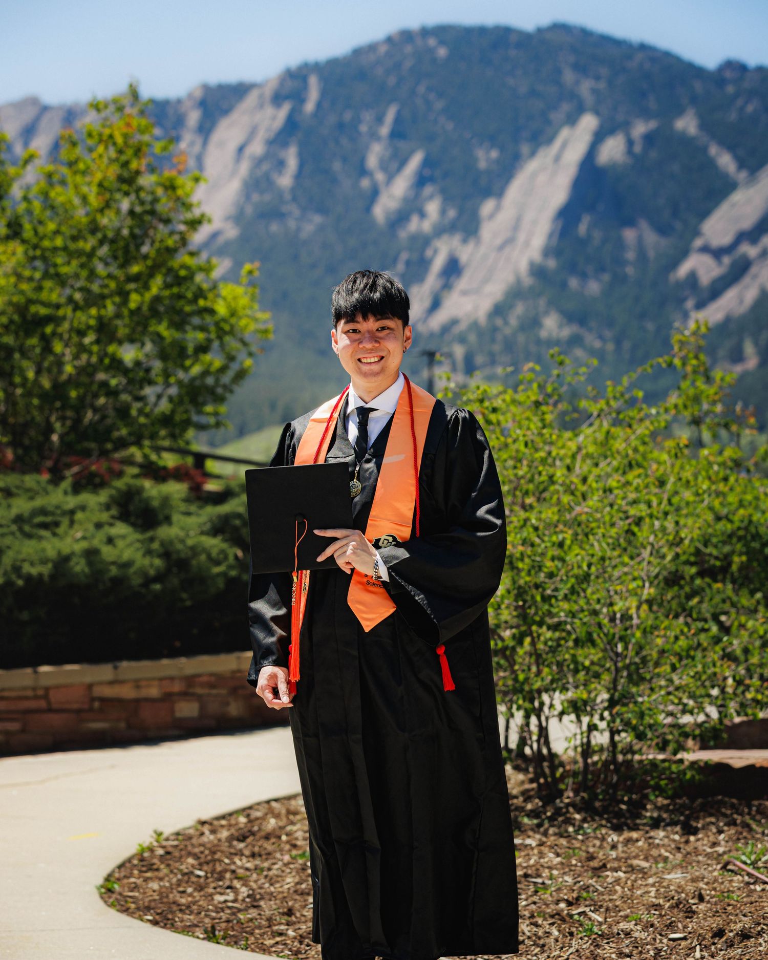 CU Boulder graduate in cap and gown with the Flatirons mountains in the background