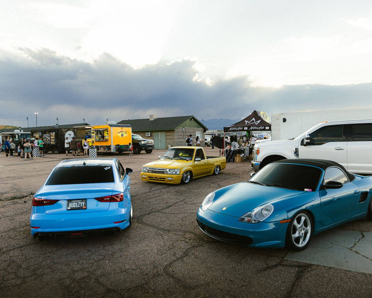 Wide angle shot of a yellow, bagged, toyota tacoma, a slammed, light blue Audi s4, and a turquoise 911 turbo s