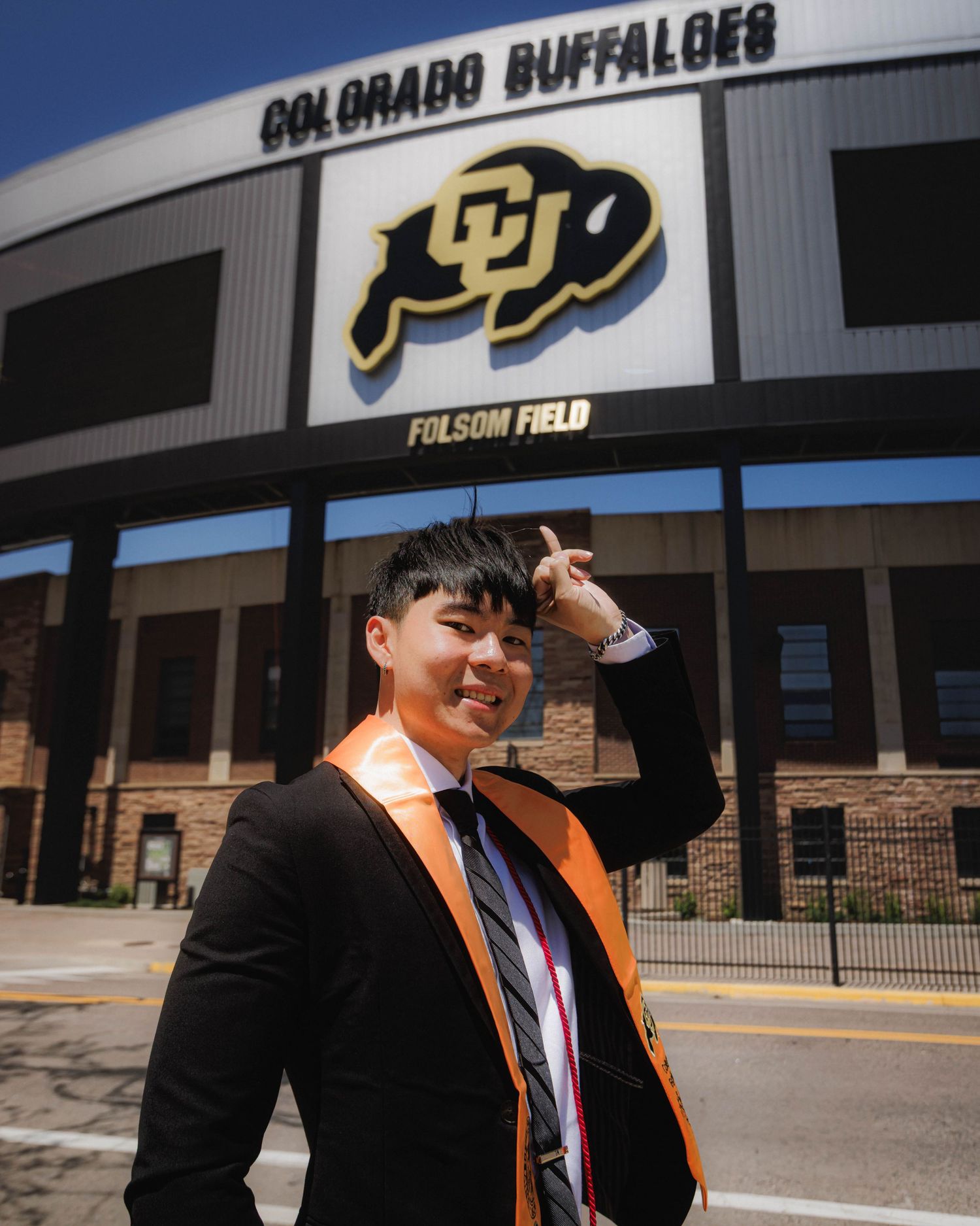 CU Boulder graduate posing with horns up in front of Folsom Field stadium