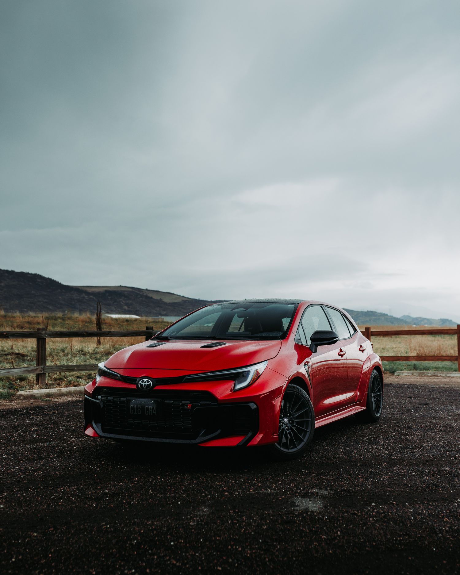 Wide angle front quarter shot of Red GR Corolla with mountains in the background during a rain storm