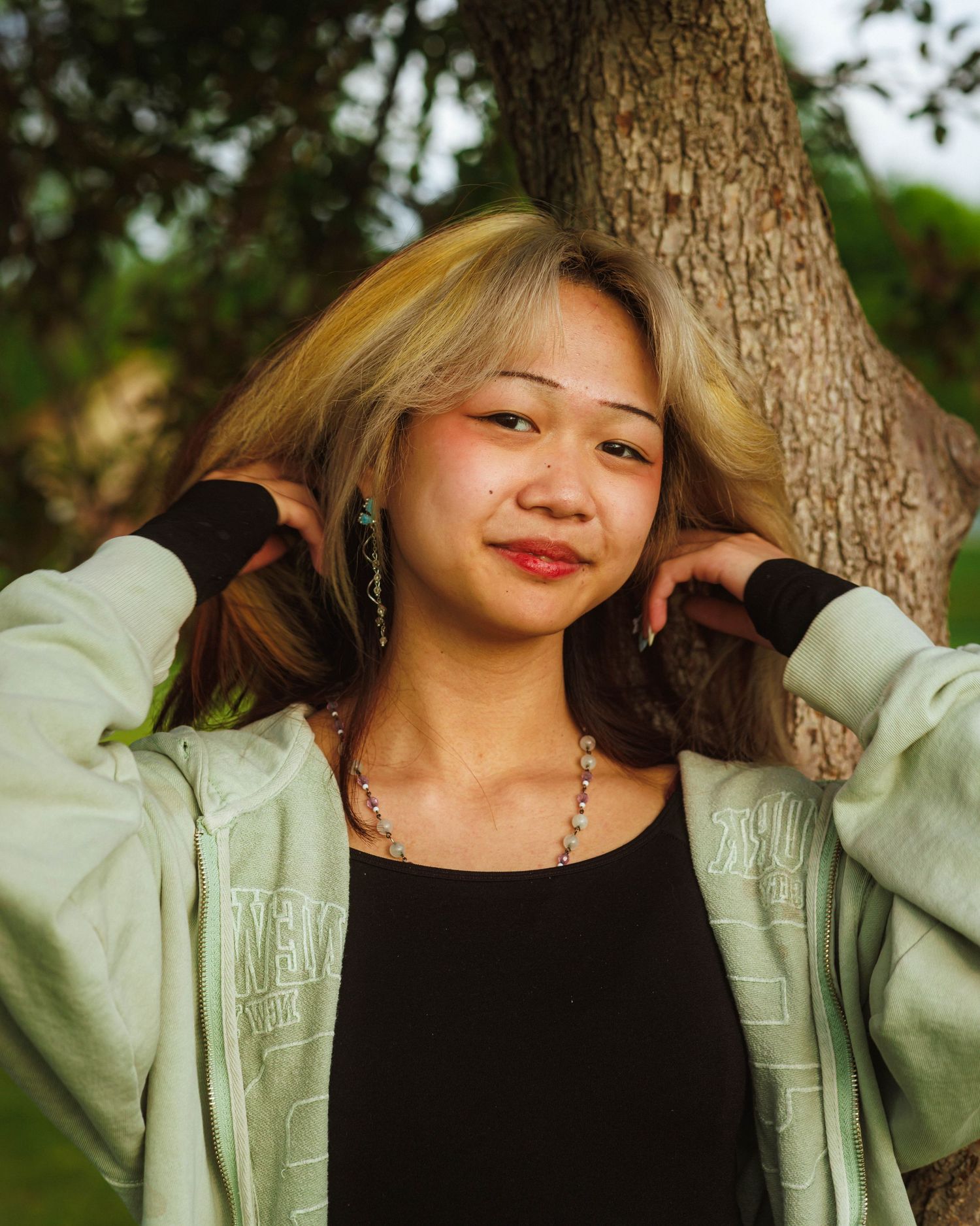 Close up senior portrait standing under a tree, playing with her hair at Arapahoe Park