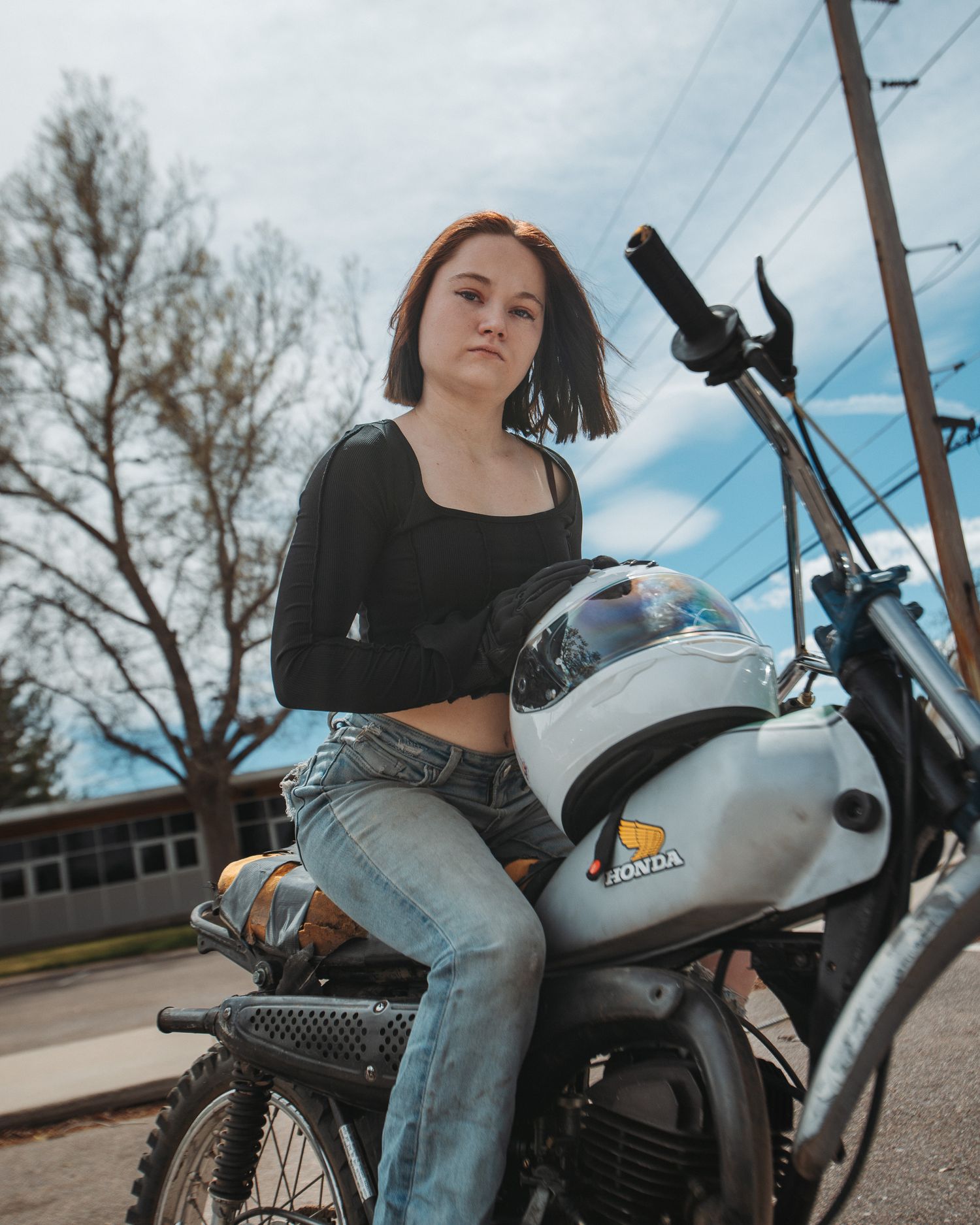 Woman straddling motorcycle with hands on gas tank, portrait session
