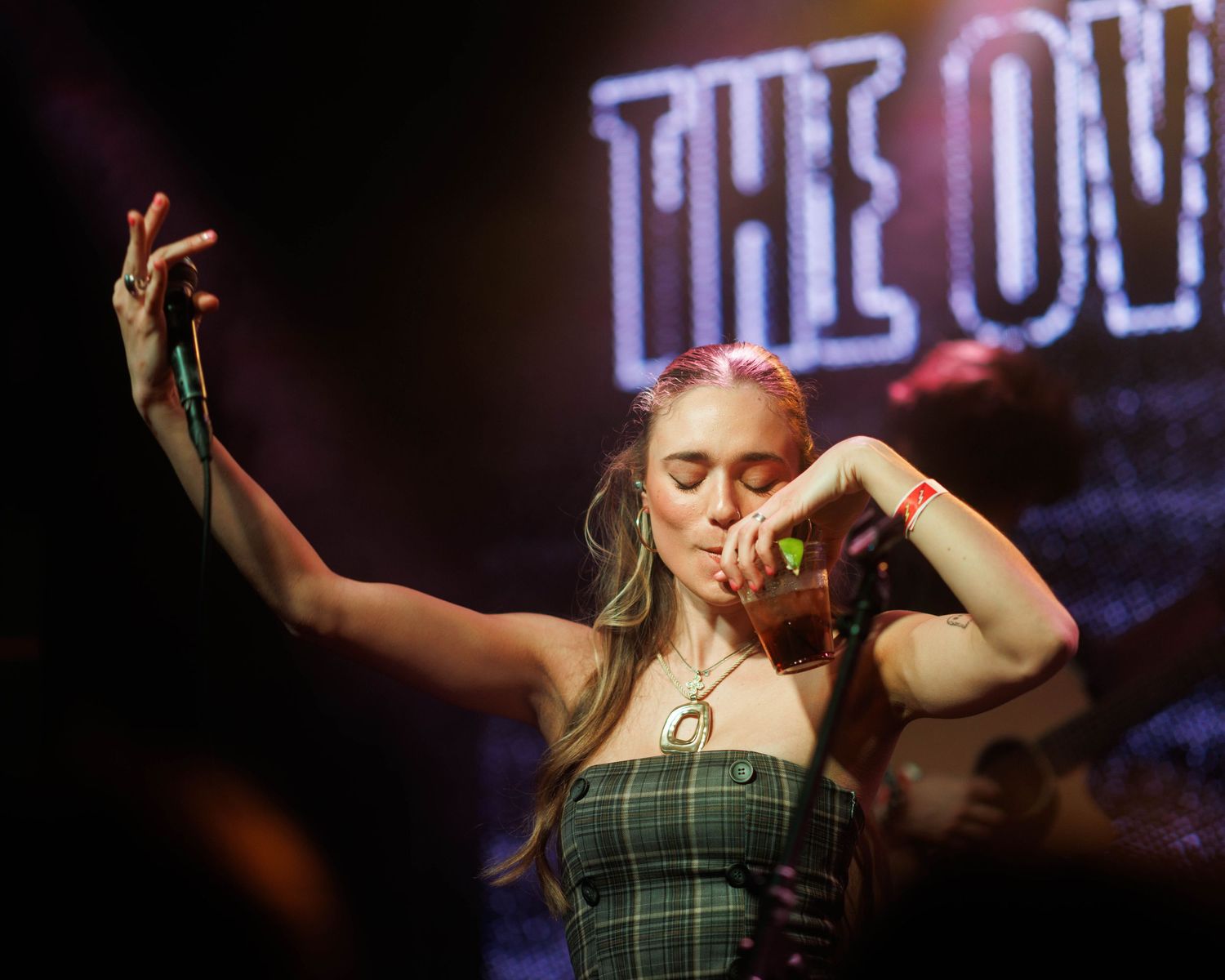 Medium shot of Kenzie Cait, taking a drink break mid set, while on The Over Nostalgic Tour at Lost Lake Denver