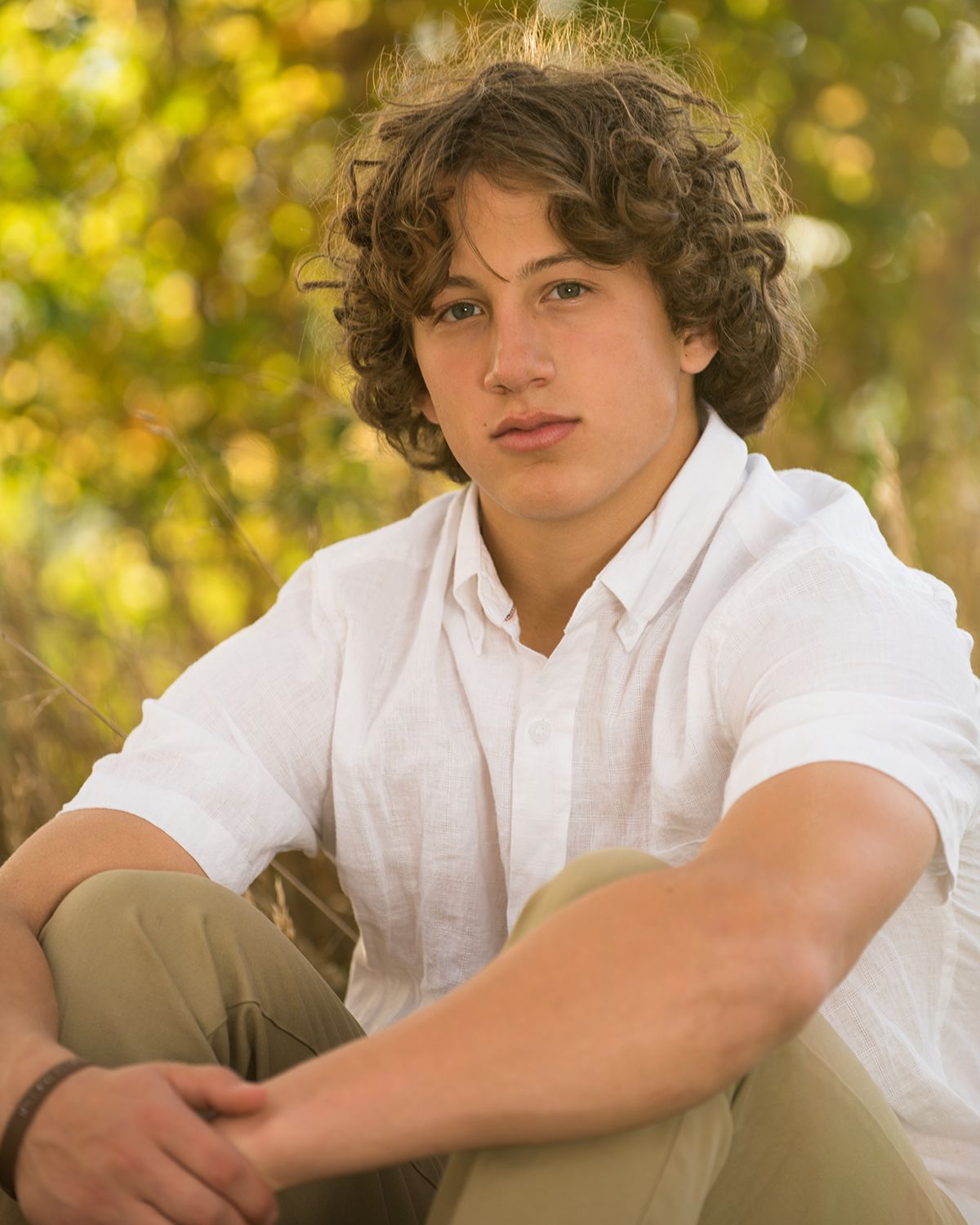 Colorado Springs senior portrait featuring a student seated among trees in golden evening light.