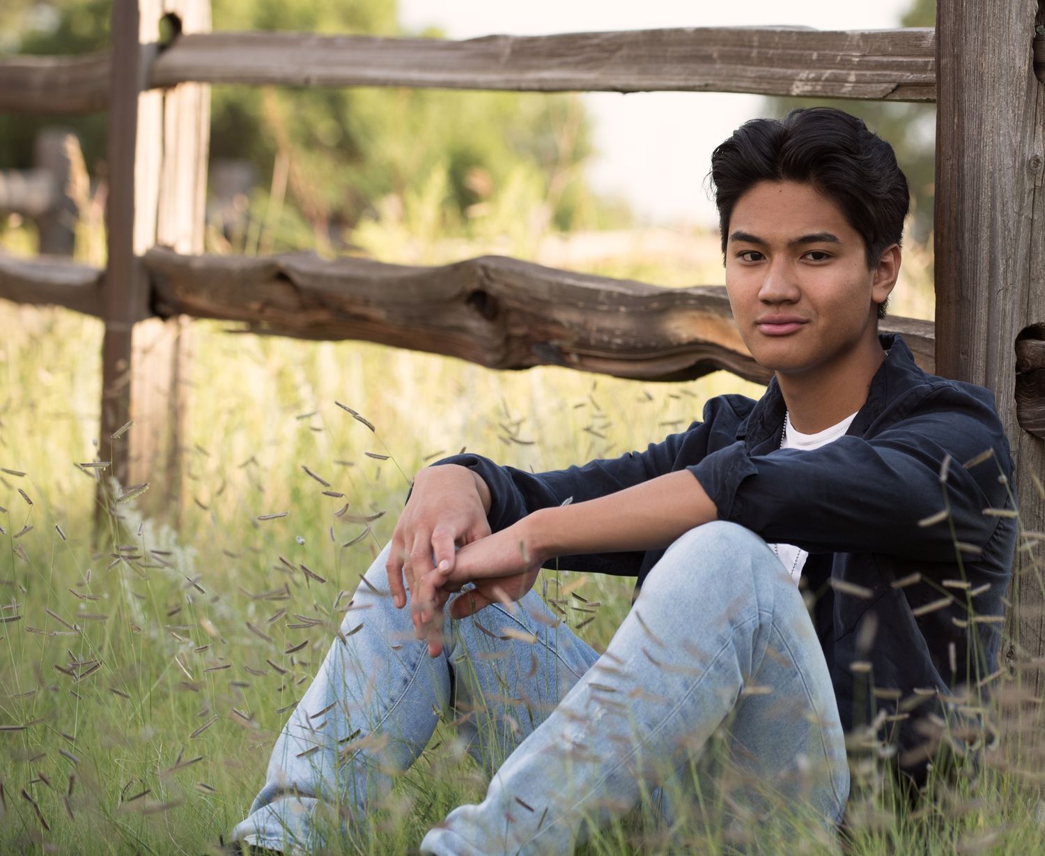 Colorado Springs senior portrait featuring a student seated beside a rustic fence in a natural outdoor setting.