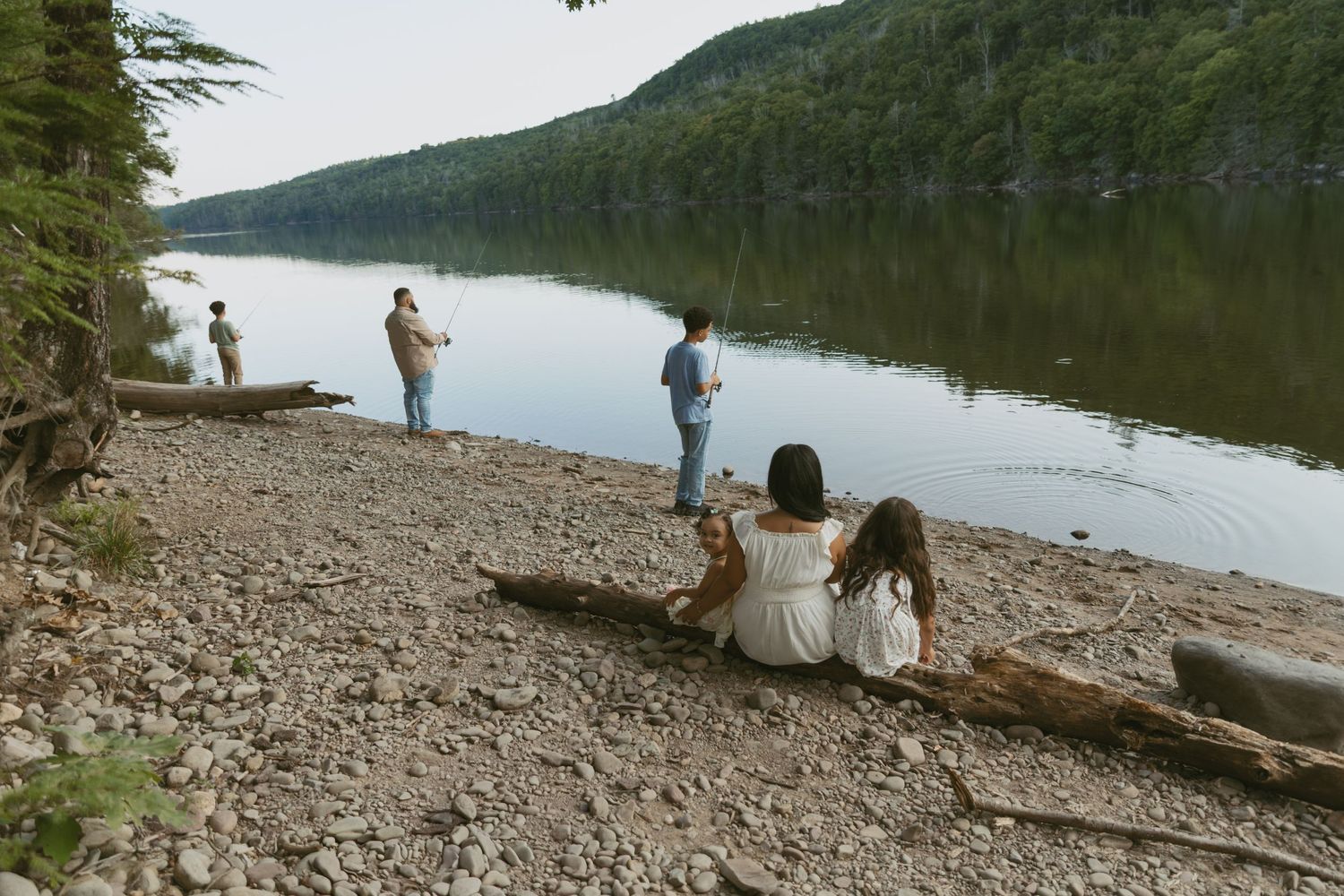 Sullivan County New York, Catskills. Family photos along the water. Family fishing while mom and daughter sit on a fallen tree and watch