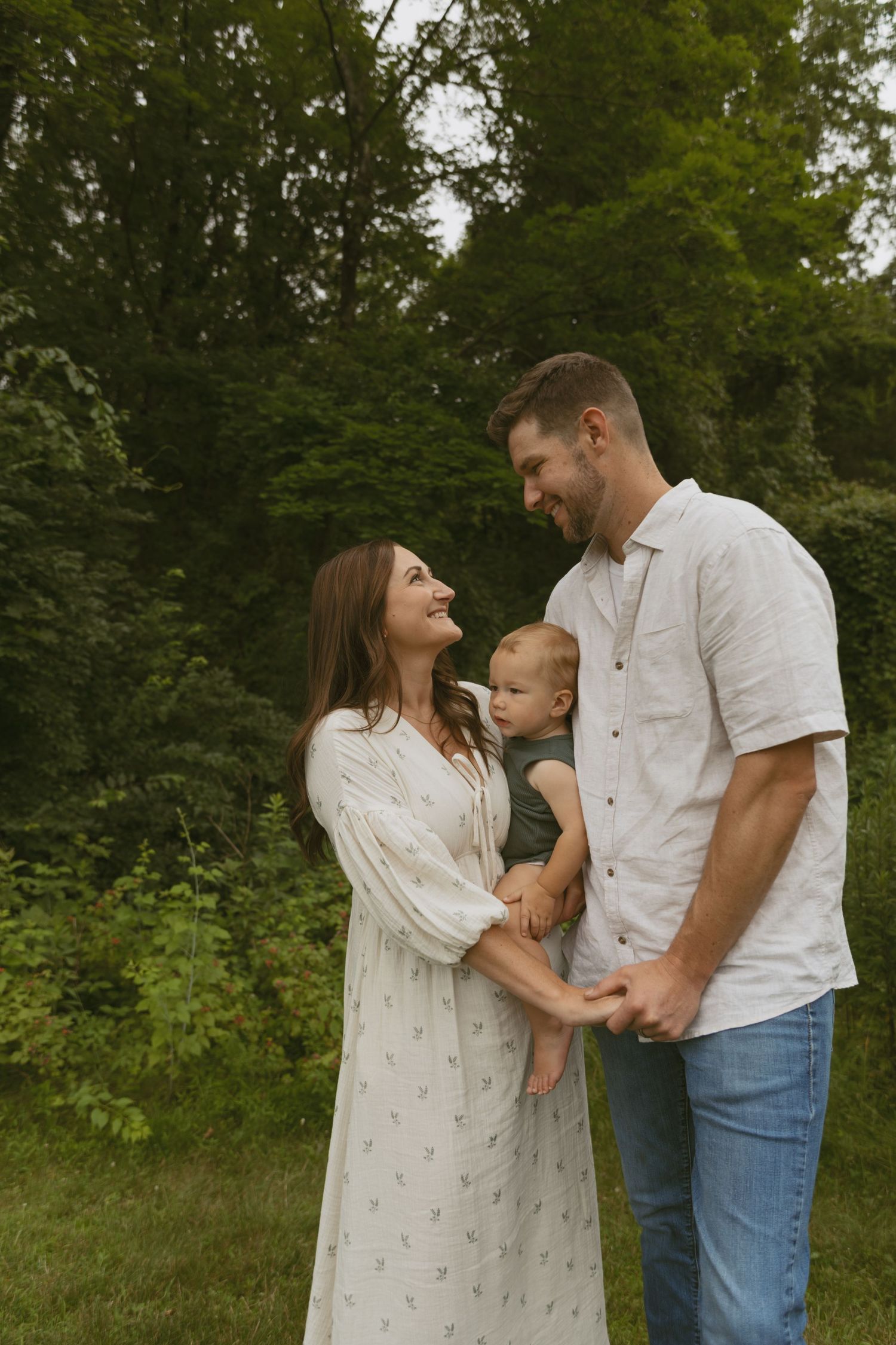 Cinematic and documentary family photos of a mom and dad looking at each other while holding their abby in a field near Milford Pennsylvania
