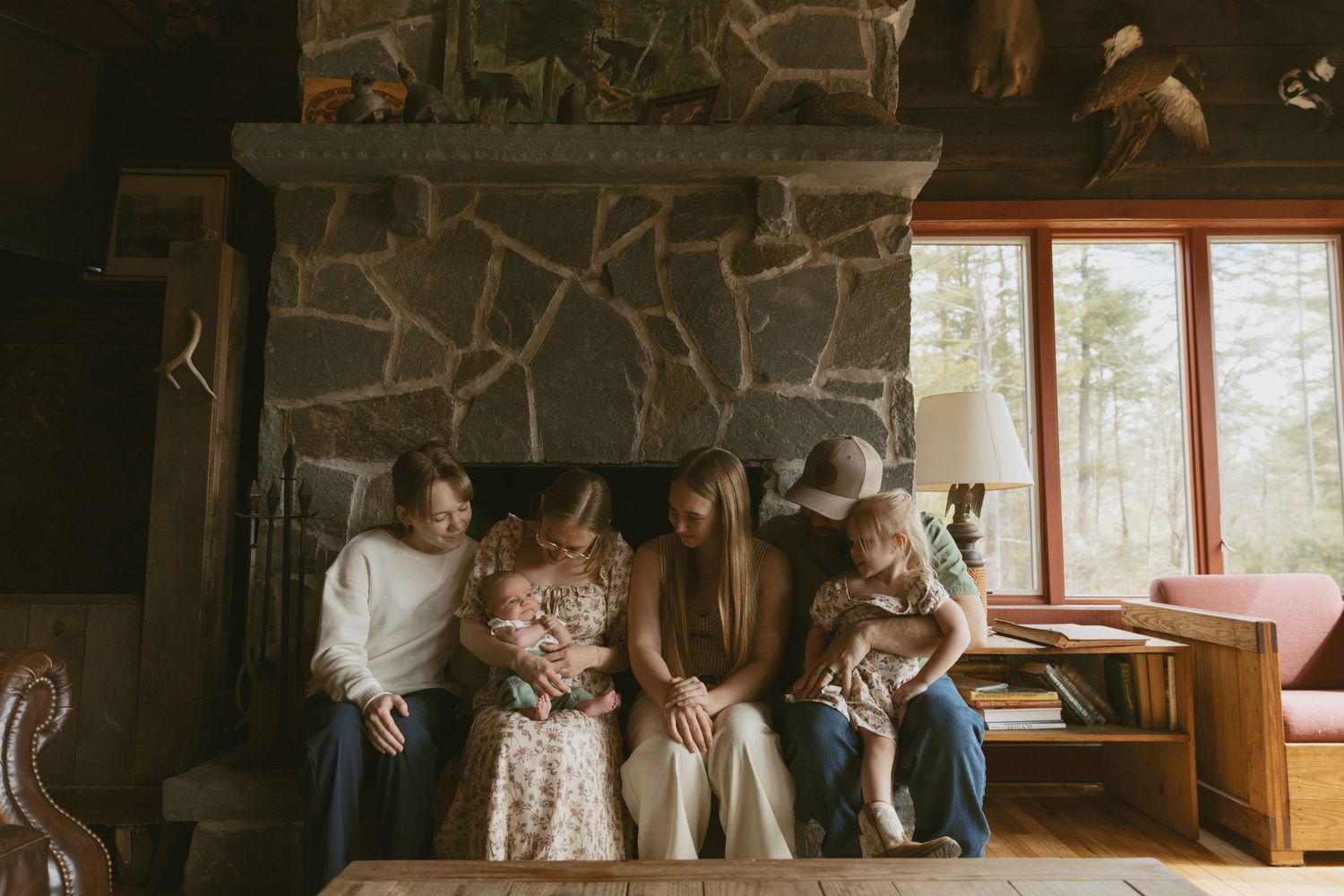 Newborn photos in family cabin in Sullivan County New York, Catskills. Family sitting together in front of the fireplace looking at newborn.