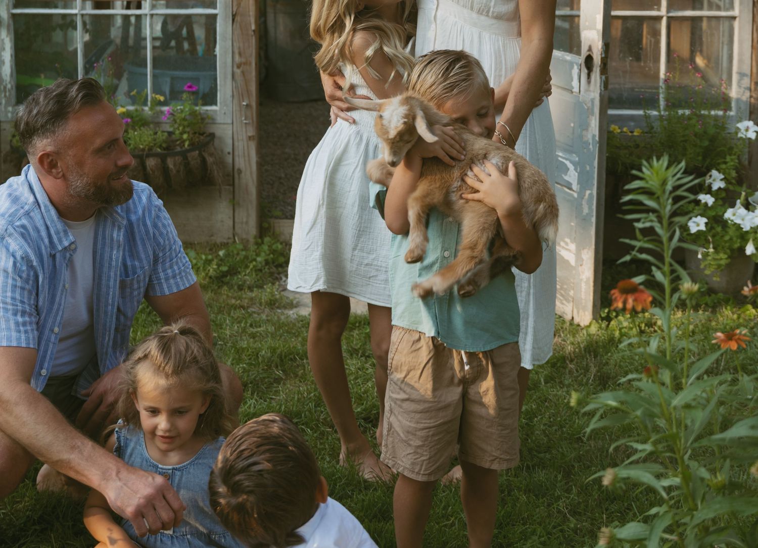 Close-up of child snuggling family goat in garden, during a backyard family photo session in Hudson Valley, New York