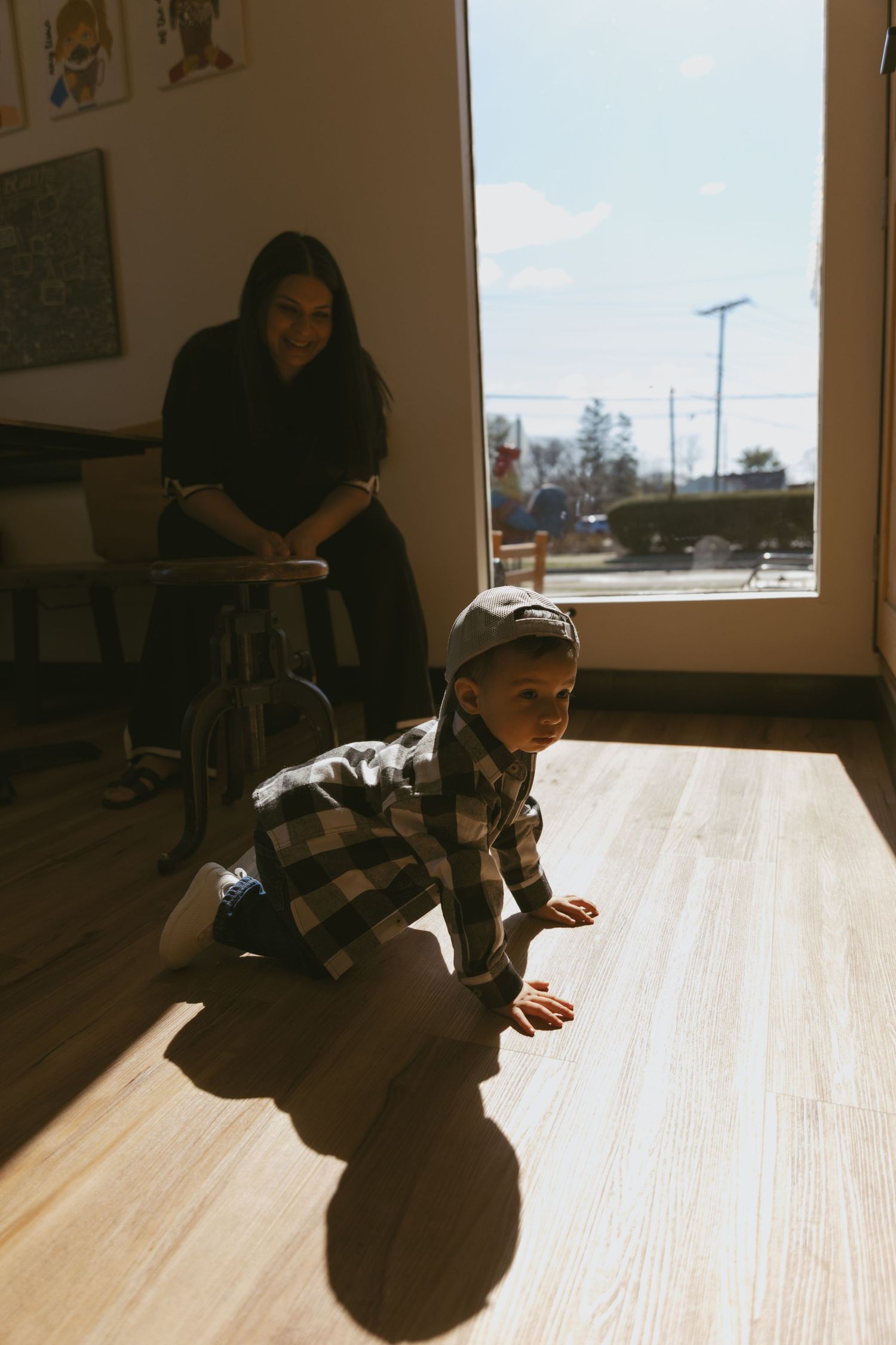 NJ family documentary lifestyle photoshoot. Toddler crawling on the floor in the sunlight coming from the window. The mom watching.