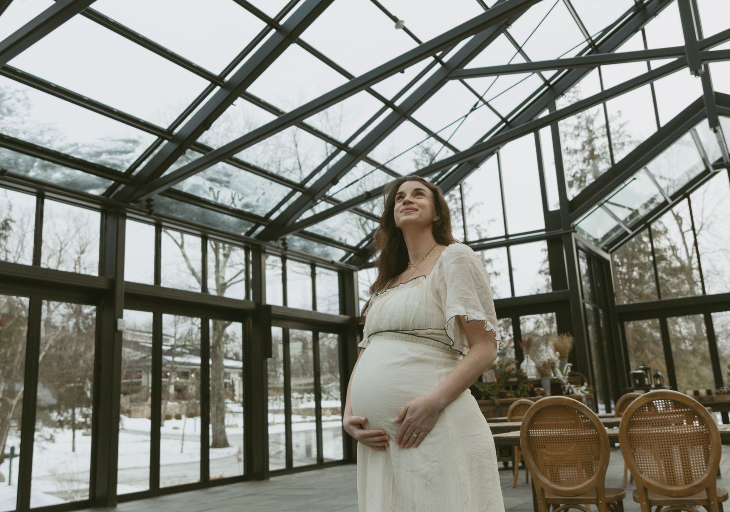 Cozy Editorial indoor maternity photos in the Glasshouse at Cedar Lake Estates in Port Jervis, New York. Mom holding baby bump by windows