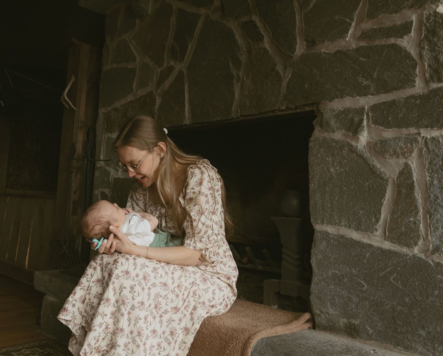 Newborn photos in family cabin in Sullivan County New York. Mom and baby sitting on fireplace ledge