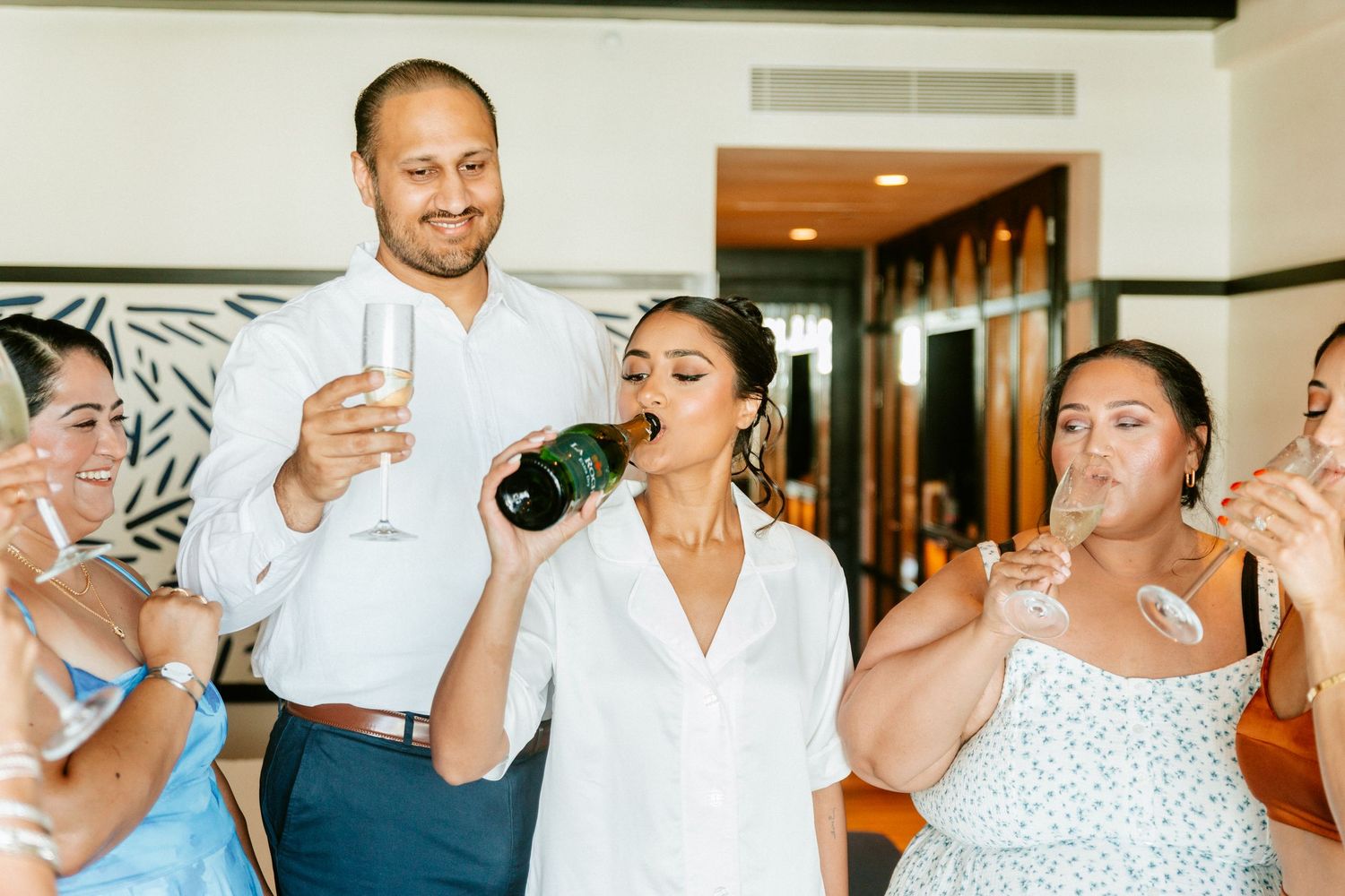 Group of friends celebrating with champagne, woman drinking from bottle at a party.
