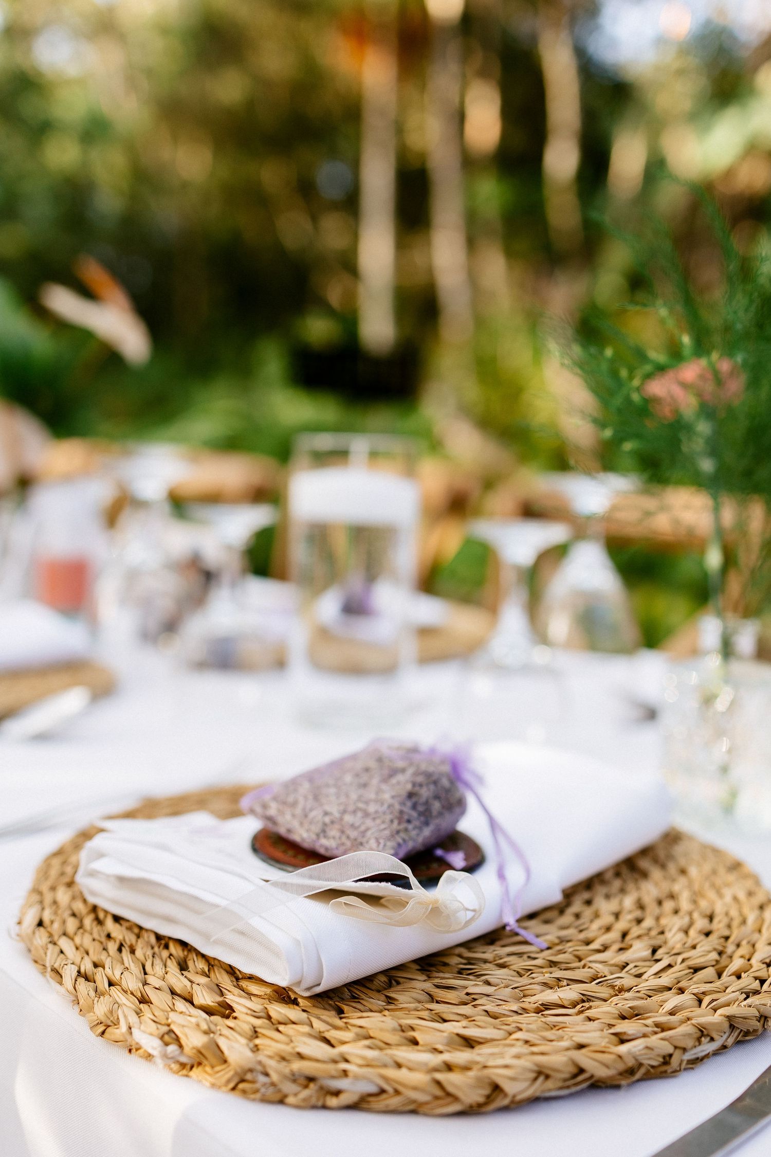 Close-up of a woven placemat with a white napkin and lavender sachet favor at an outdoor wedding.