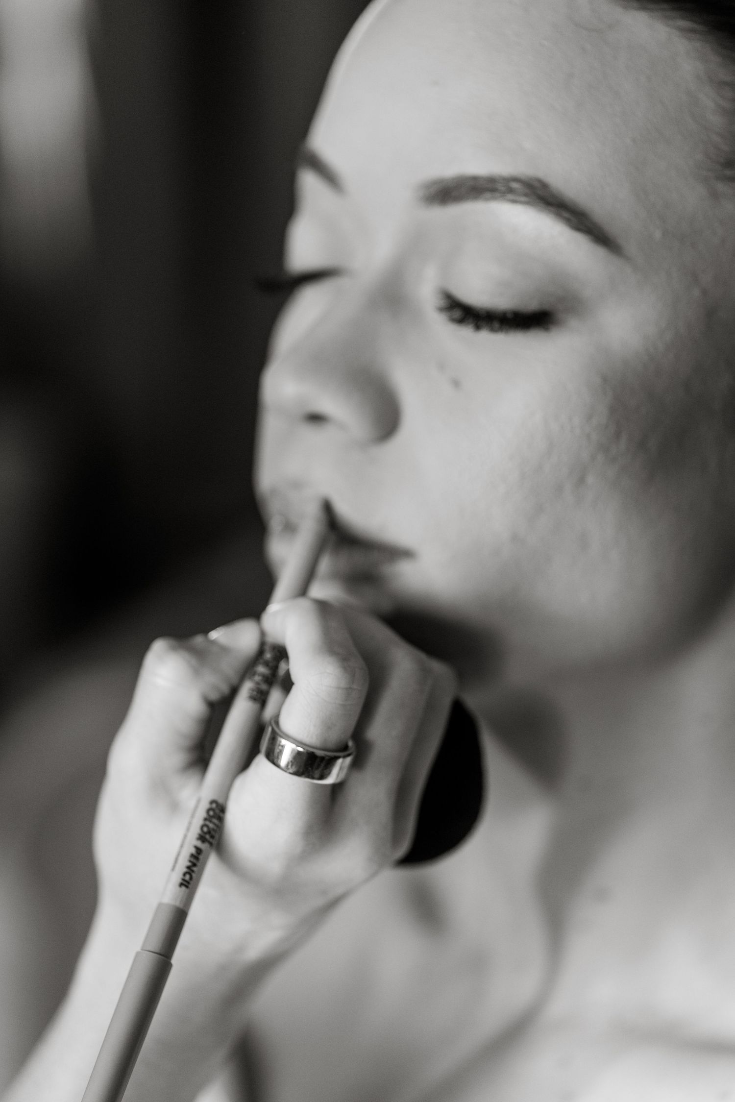Black and white portrait of bride getting lip makeup applied during wedding day preparation.