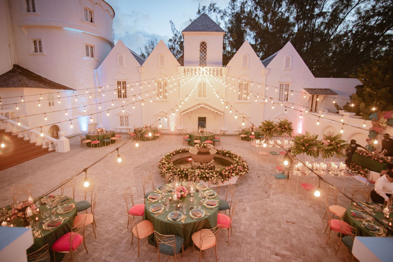 Elegant outdoor wedding reception at a white castle venue with string lights, floral centerpieces, and colorful table settings.