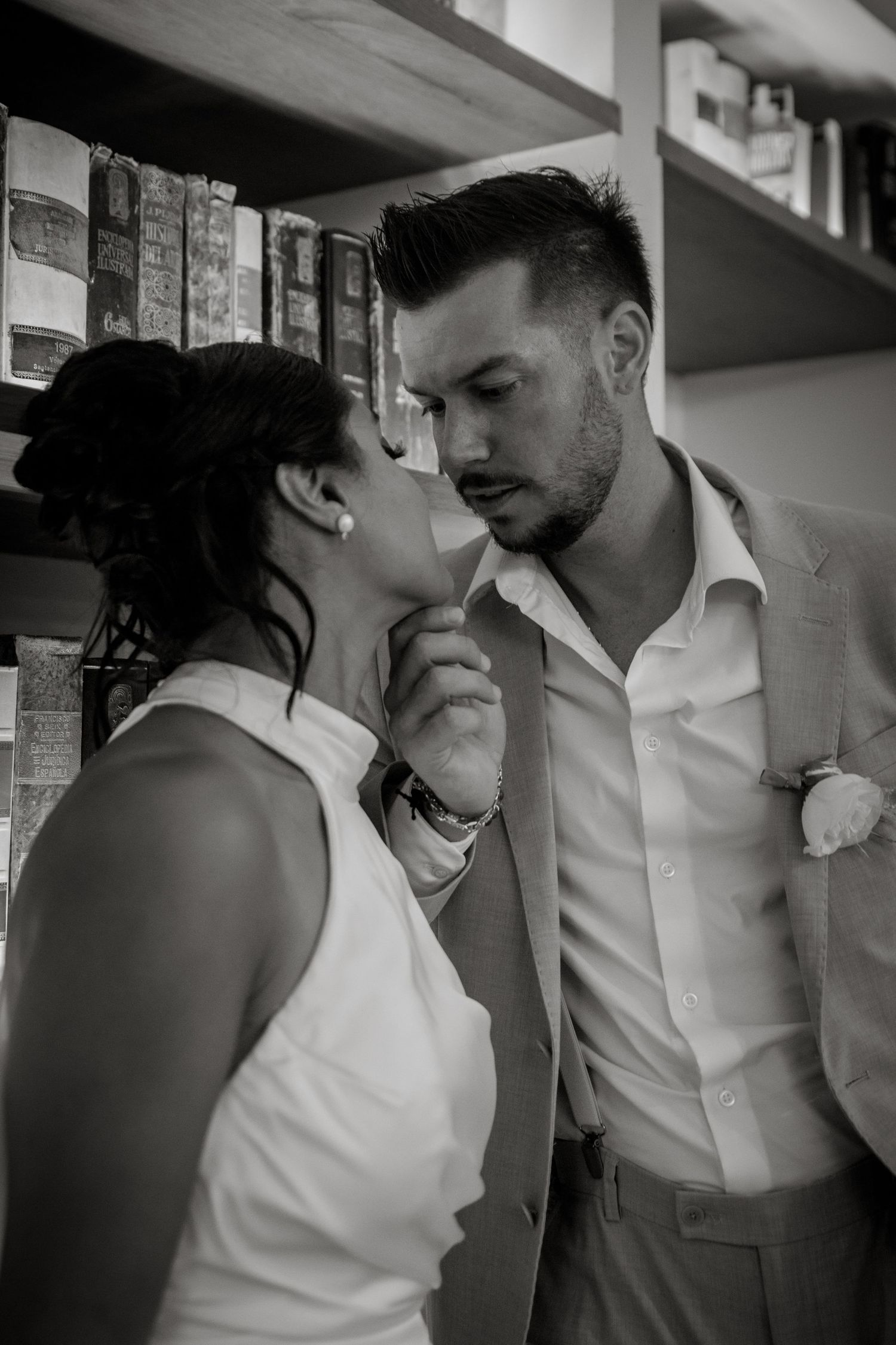 Black and white portrait of bride and groom sharing intimate moment near bookshelves.