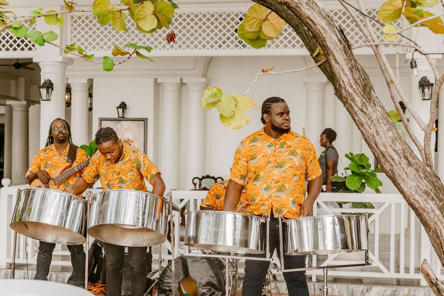 Three musicians in orange floral shirts playing steel drums at an outdoor Caribbean wedding reception.