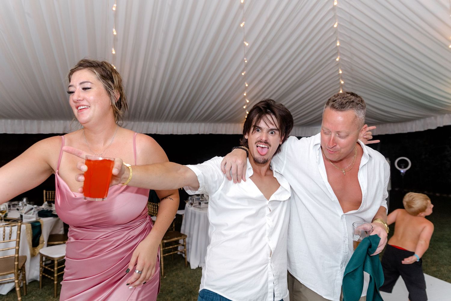 Three wedding guests laughing and dancing together at a festive reception.