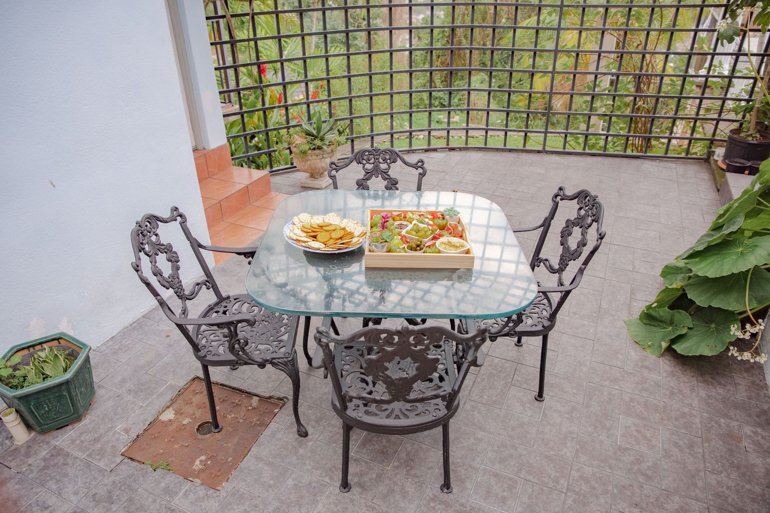 Ornate black iron patio table with fruit displays on stone terrace surrounded by lush garden greenery.