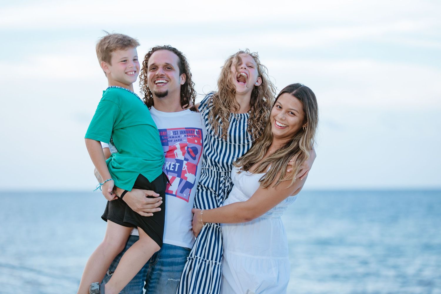 Happy family of four laughing and posing together on a beautiful beach at sunset.