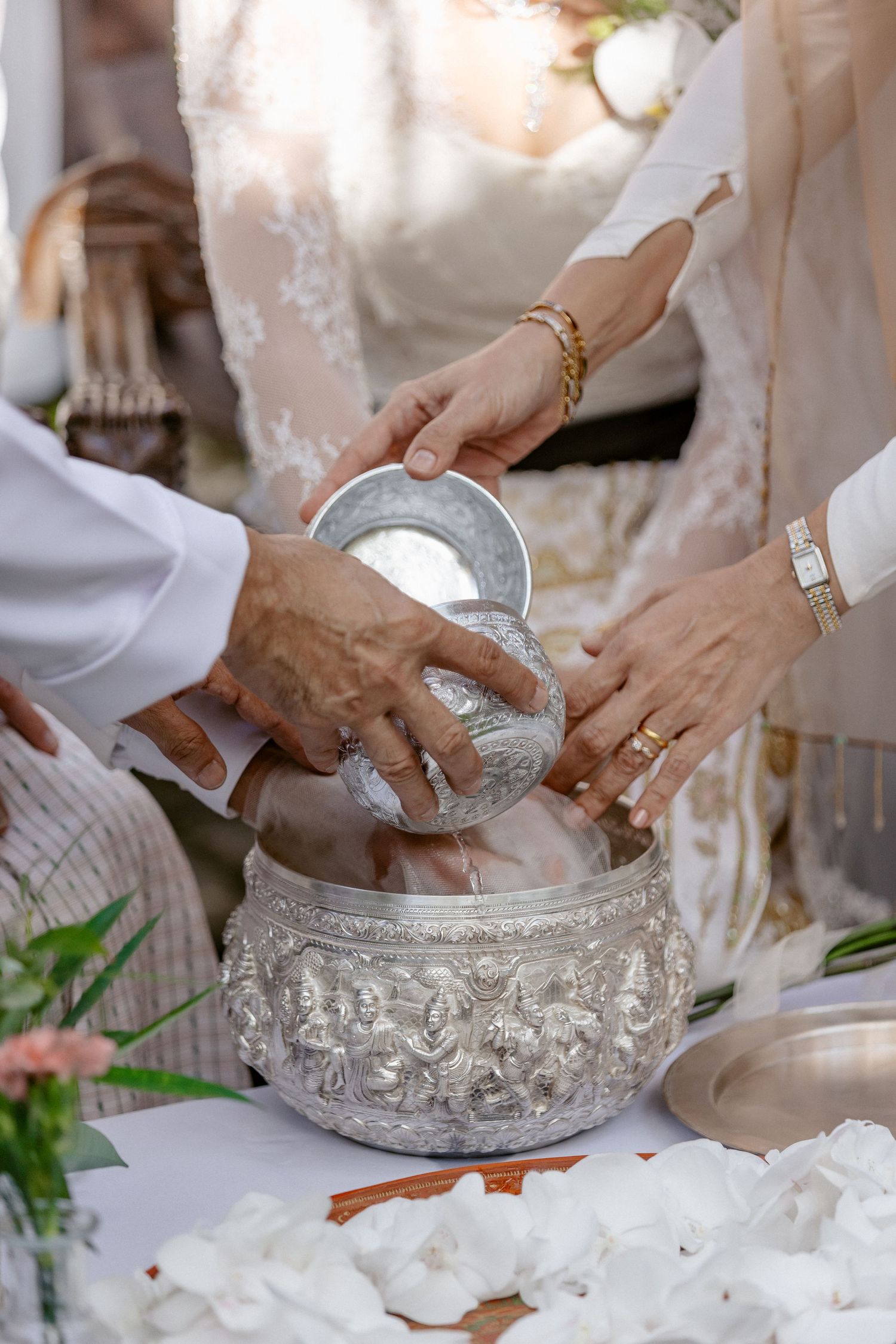 Hands reaching into ornate silver bowl during traditional Thai wedding water blessing ceremony.