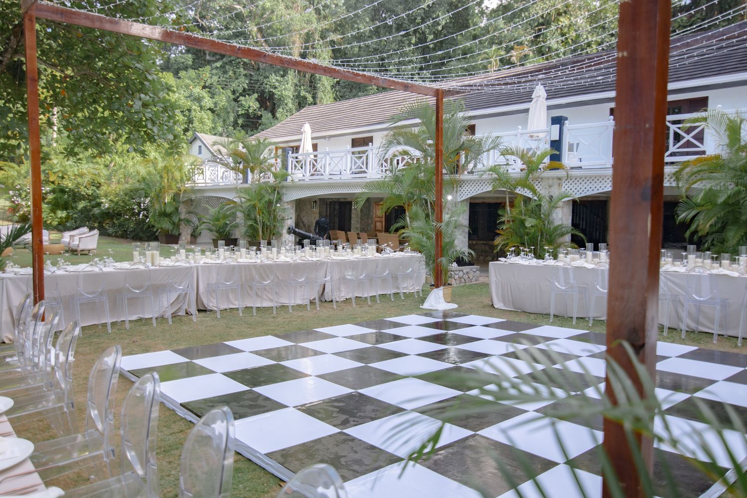 Elegant outdoor wedding reception with black and white checkered dance floor, white-draped tables, and lush garden setting.
