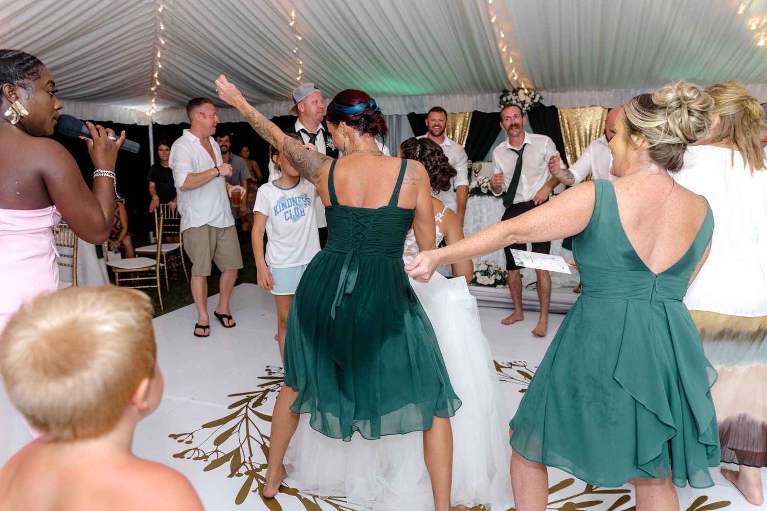 Bride and guests dancing energetically on a decorated white floor at a wedding.