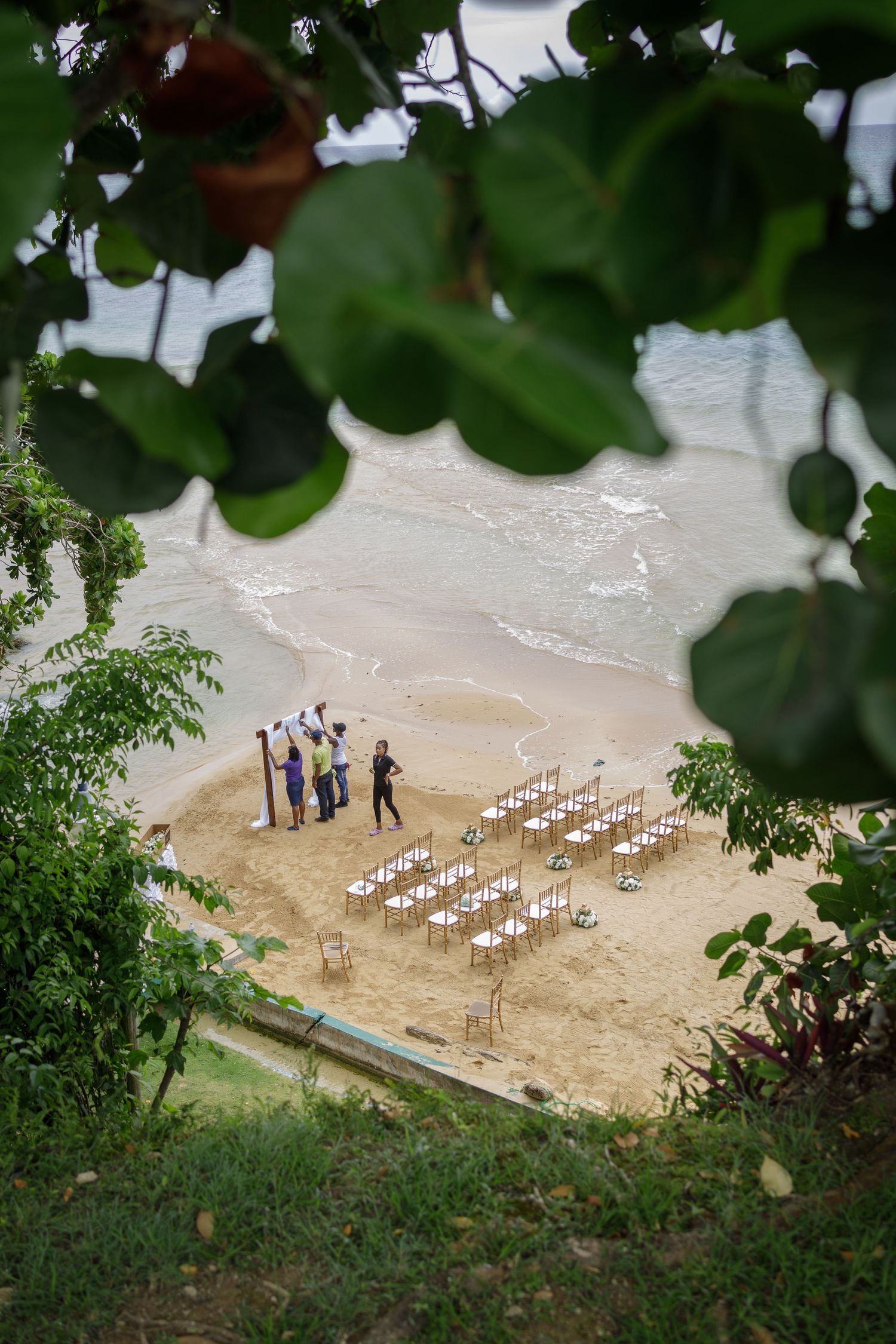 Aerial view of beach wedding ceremony setup with white chairs on sand.