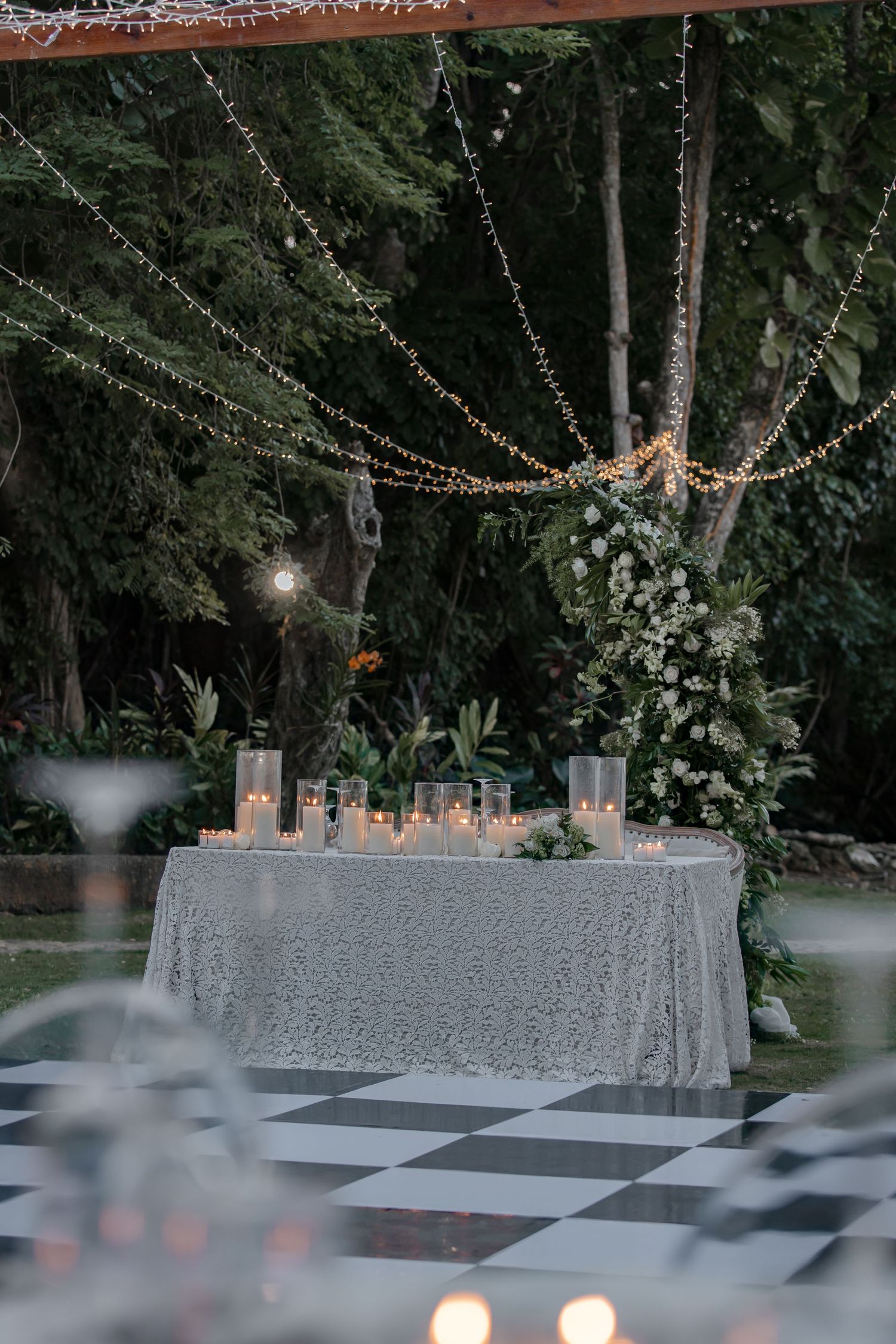 Romantic outdoor wedding sweetheart table with candles and fairy lights over a checkered dance floor.