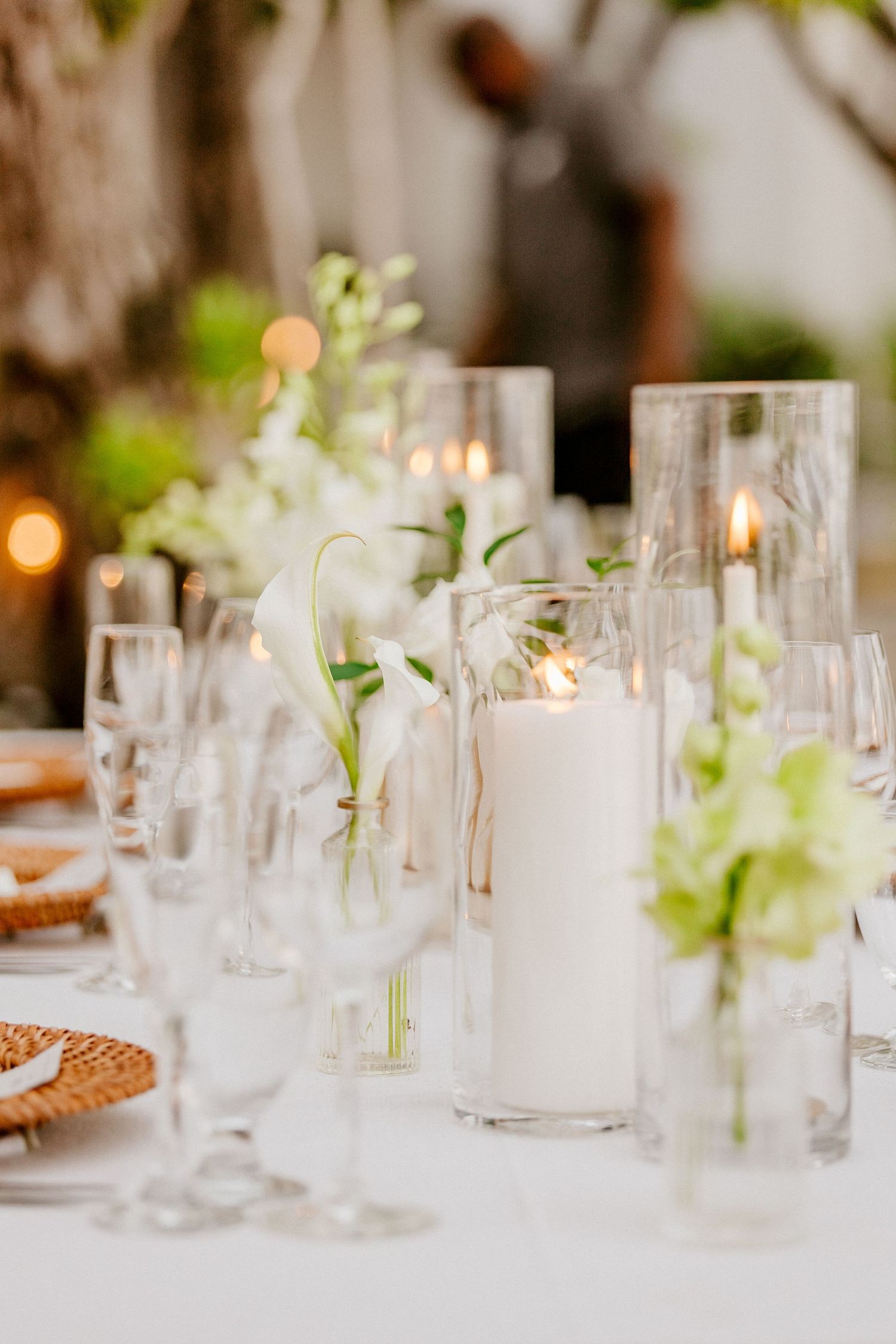Romantic wedding tablescape with white pillar candles, green and white floral arrangements, and crystal glassware at dusk.