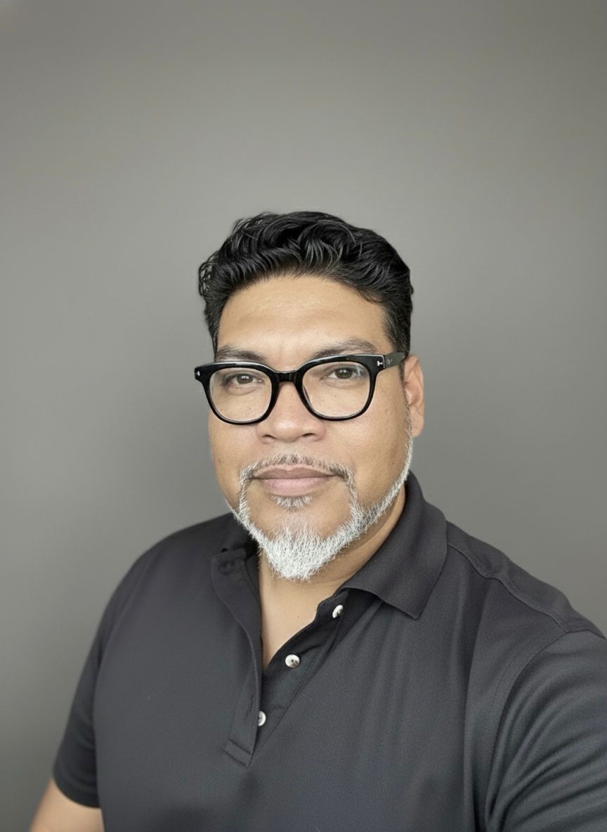 Middle-aged man with salt-and-pepper beard wearing black glasses and polo shirt poses for professional headshot.