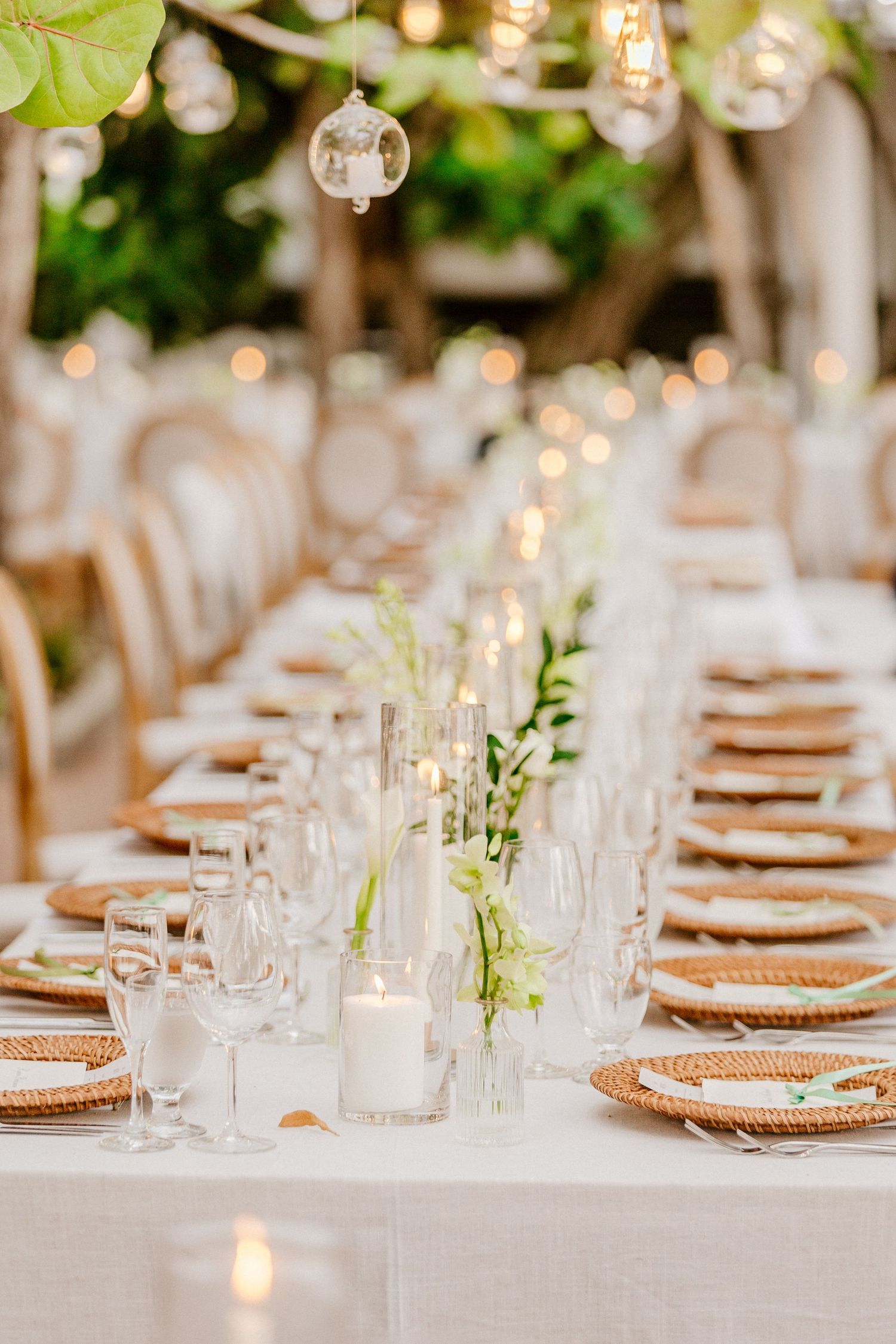 Elegant outdoor wedding reception table with woven charger plates, crystal glasses, white candles, and floral centerpieces.
