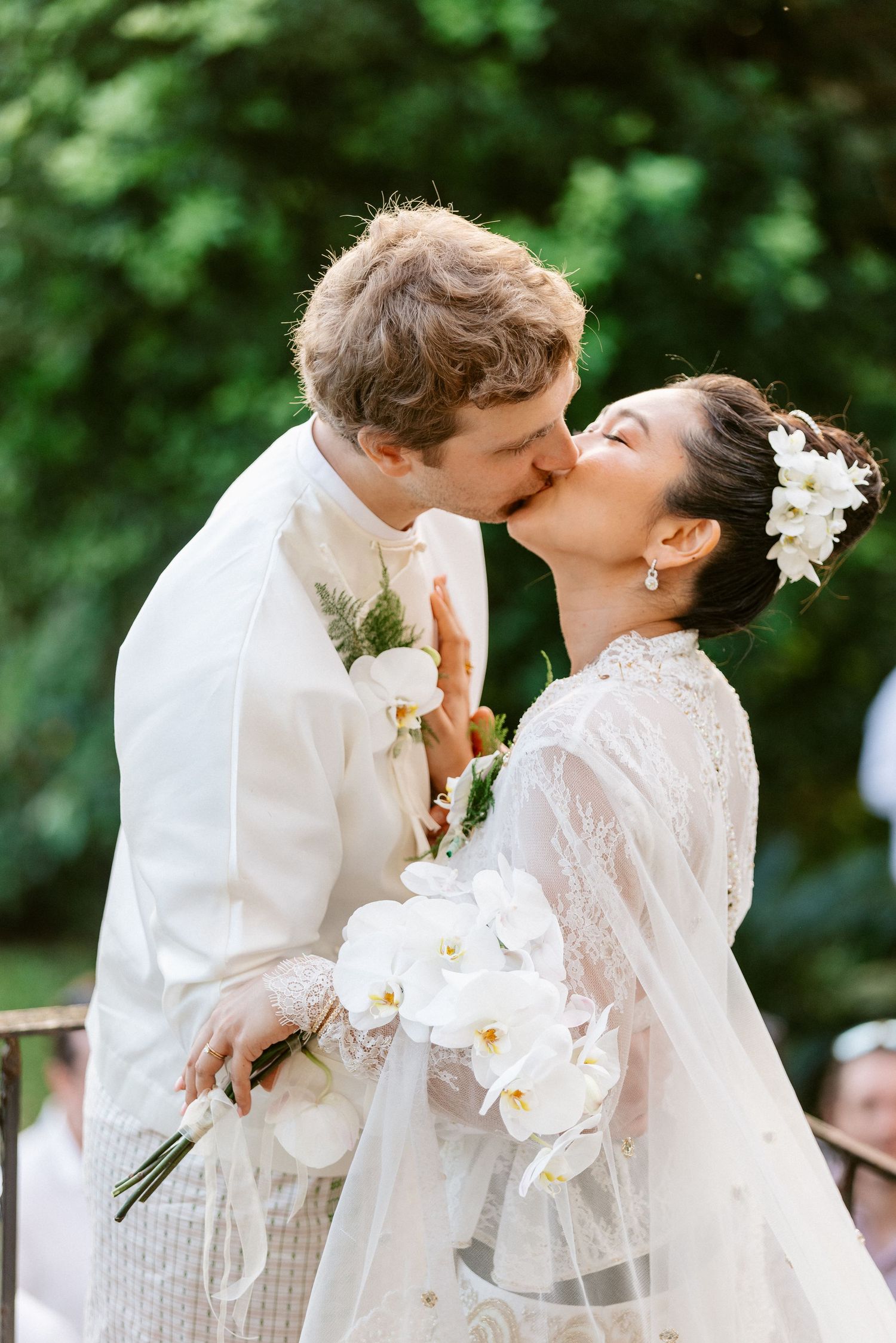 Bride and groom share a kiss at the altar, bride holding white orchid bouquet during outdoor ceremony.