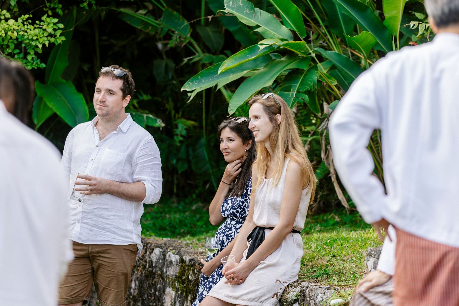 Group of people sitting outdoors near tropical plants at a casual garden gathering.