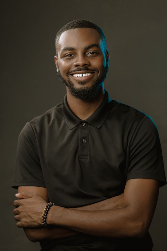 Smiling young Black man in dark polo shirt with arms crossed poses for studio portrait headshot.