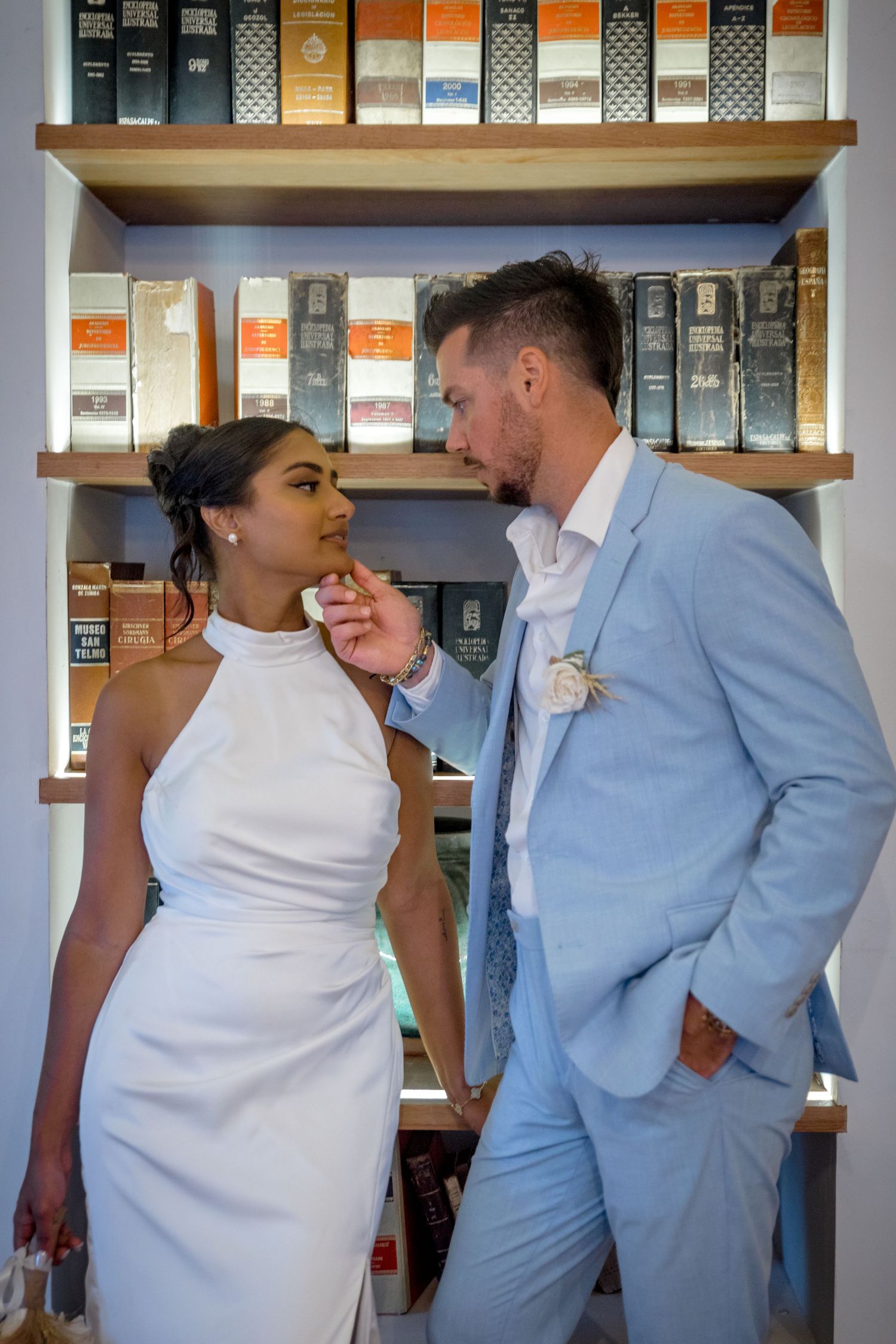 Bride and groom share intimate moment in front of shelves at wedding reception venue.