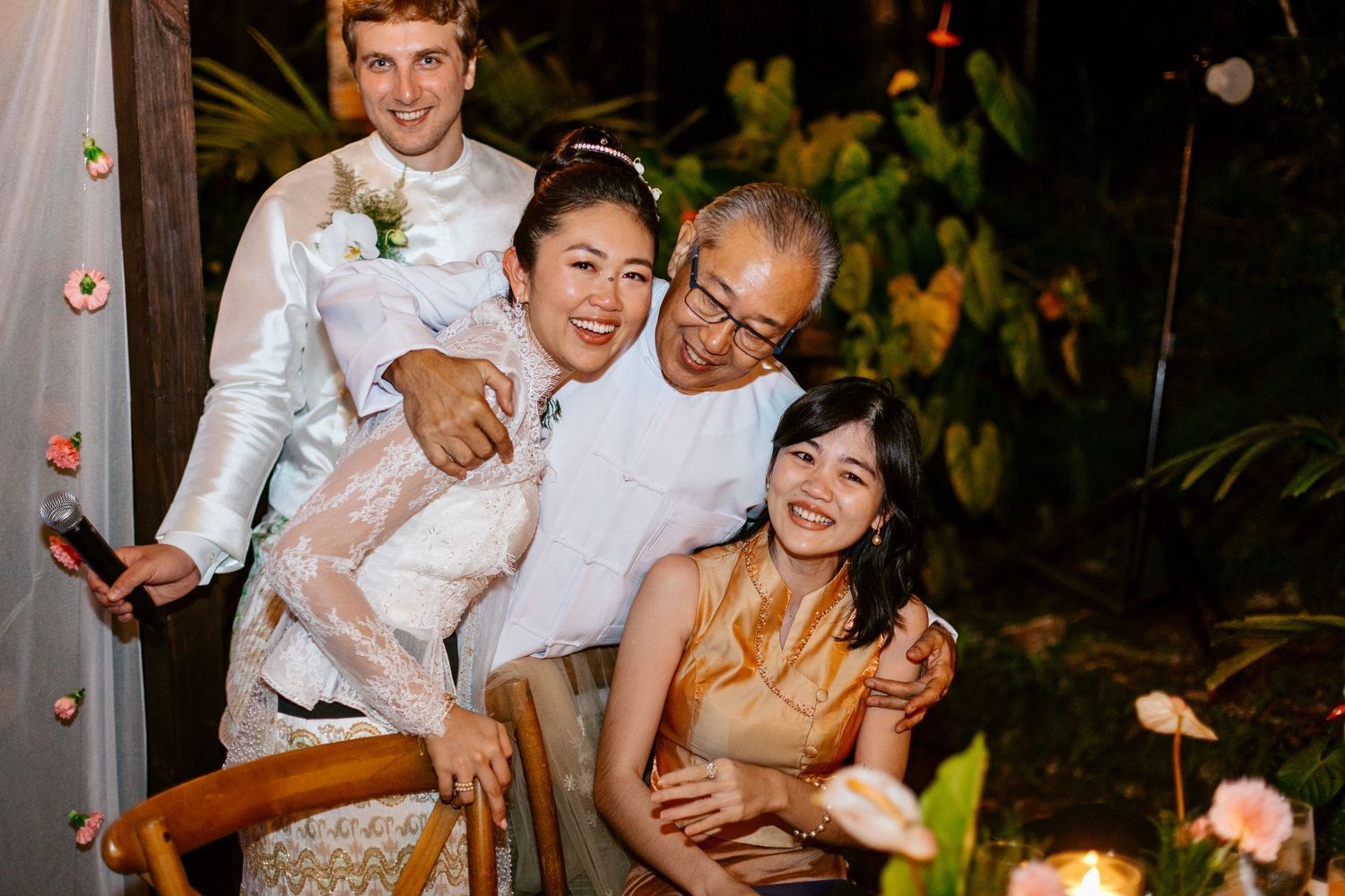 Happy family of four posing together at nighttime outdoor wedding celebration.