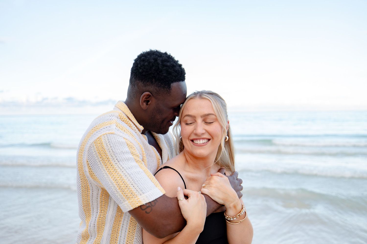 Smiling interracial couple embracing romantically on a serene tropical beach.