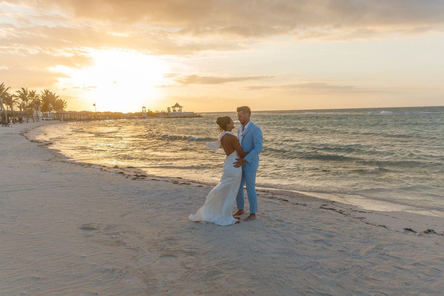 Couple sharing a romantic moment on a sandy beach at sunset during their destination wedding ceremony.