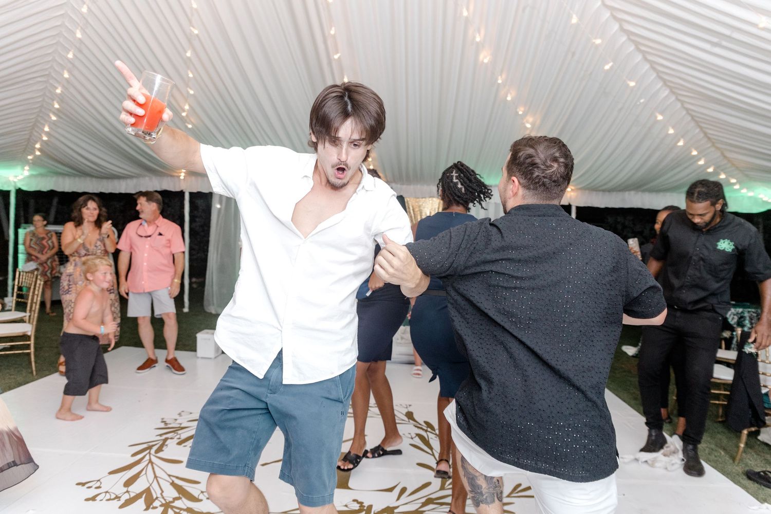 Young man in white shirt dancing expressively at an elegant wedding reception.