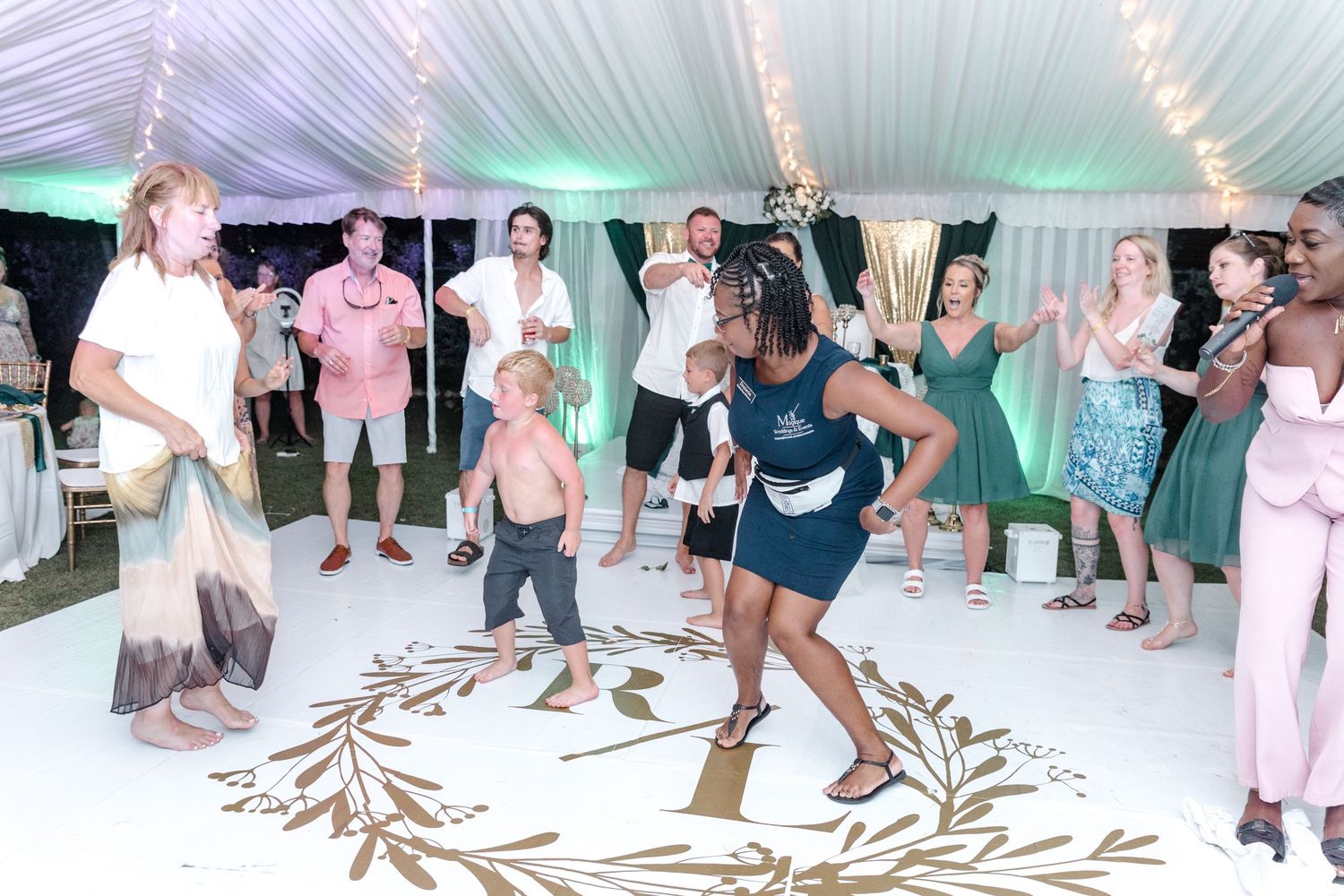 Guests dancing joyfully at a wedding reception under a white tent with string lights.