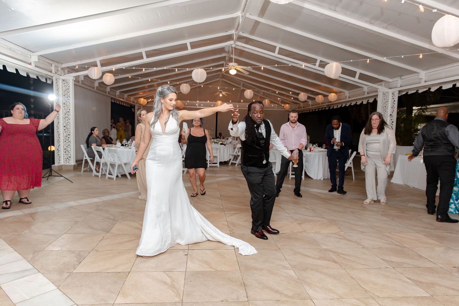 Bride in white gown and groom dance together as wedding guests watch under elegant tent venue.