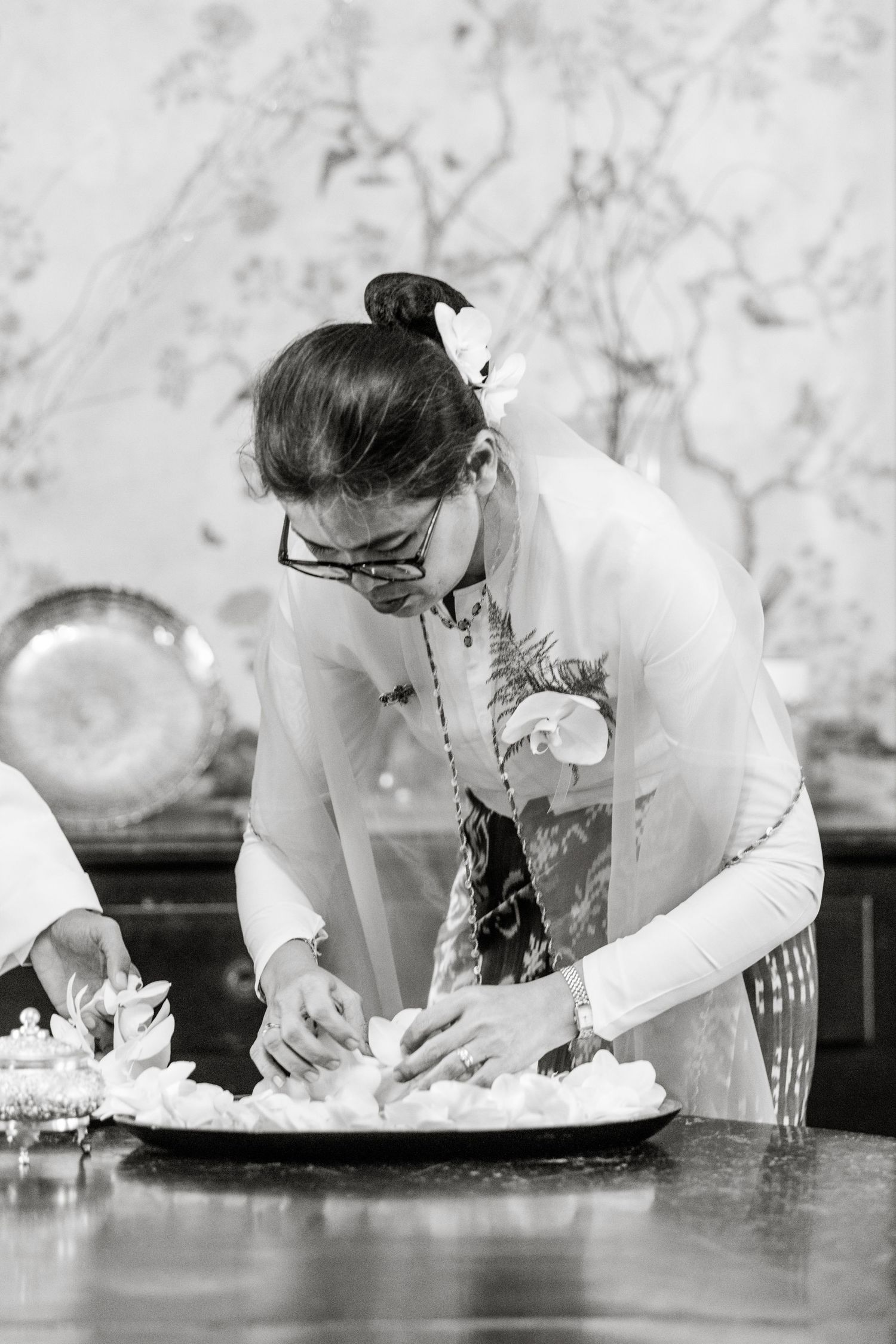 Black and white photo of a woman in traditional attire preparing food on a tray at a ceremonial table.