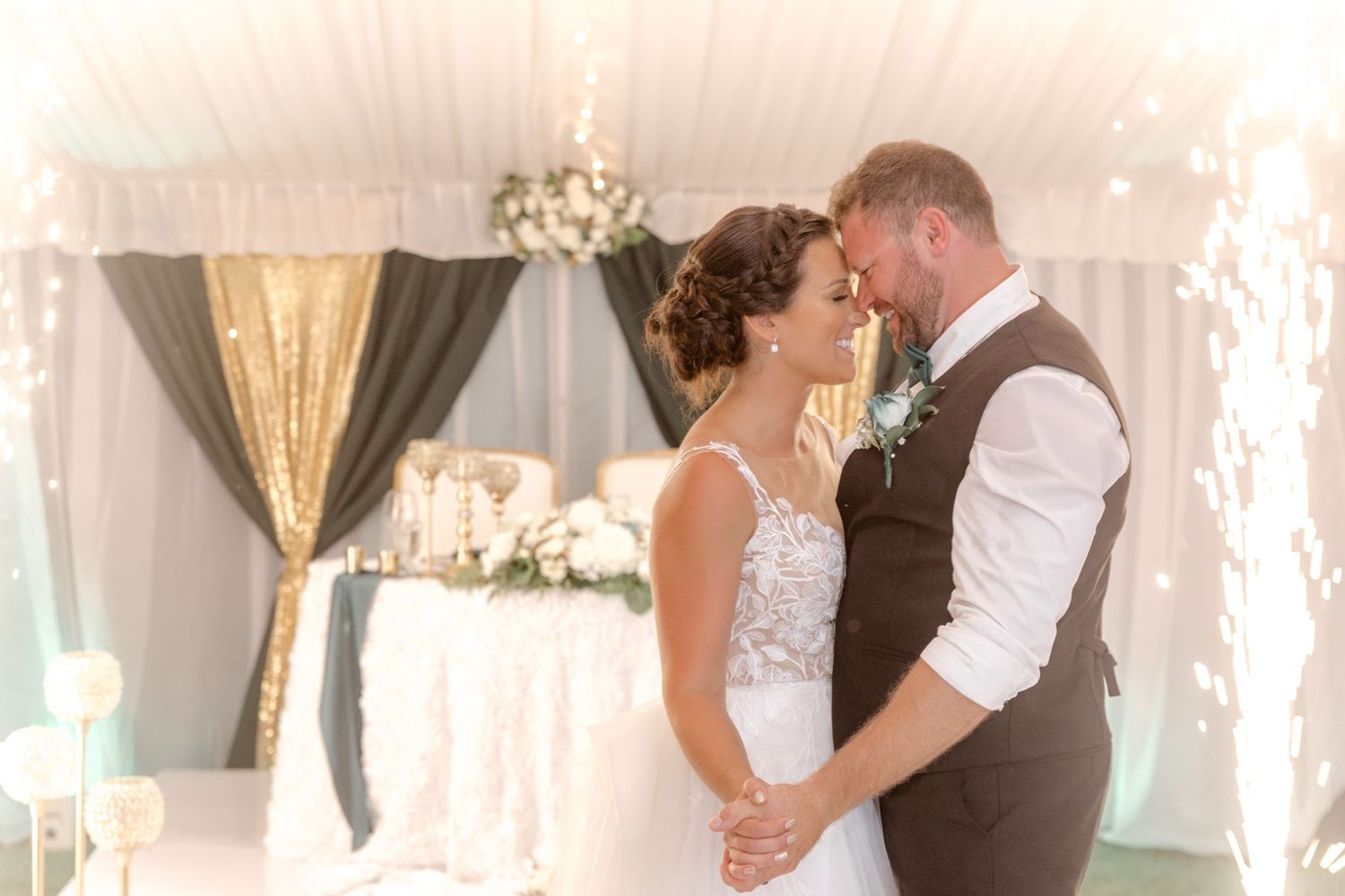 Newlyweds sharing a tender forehead touch under sparkling lights at their wedding reception.